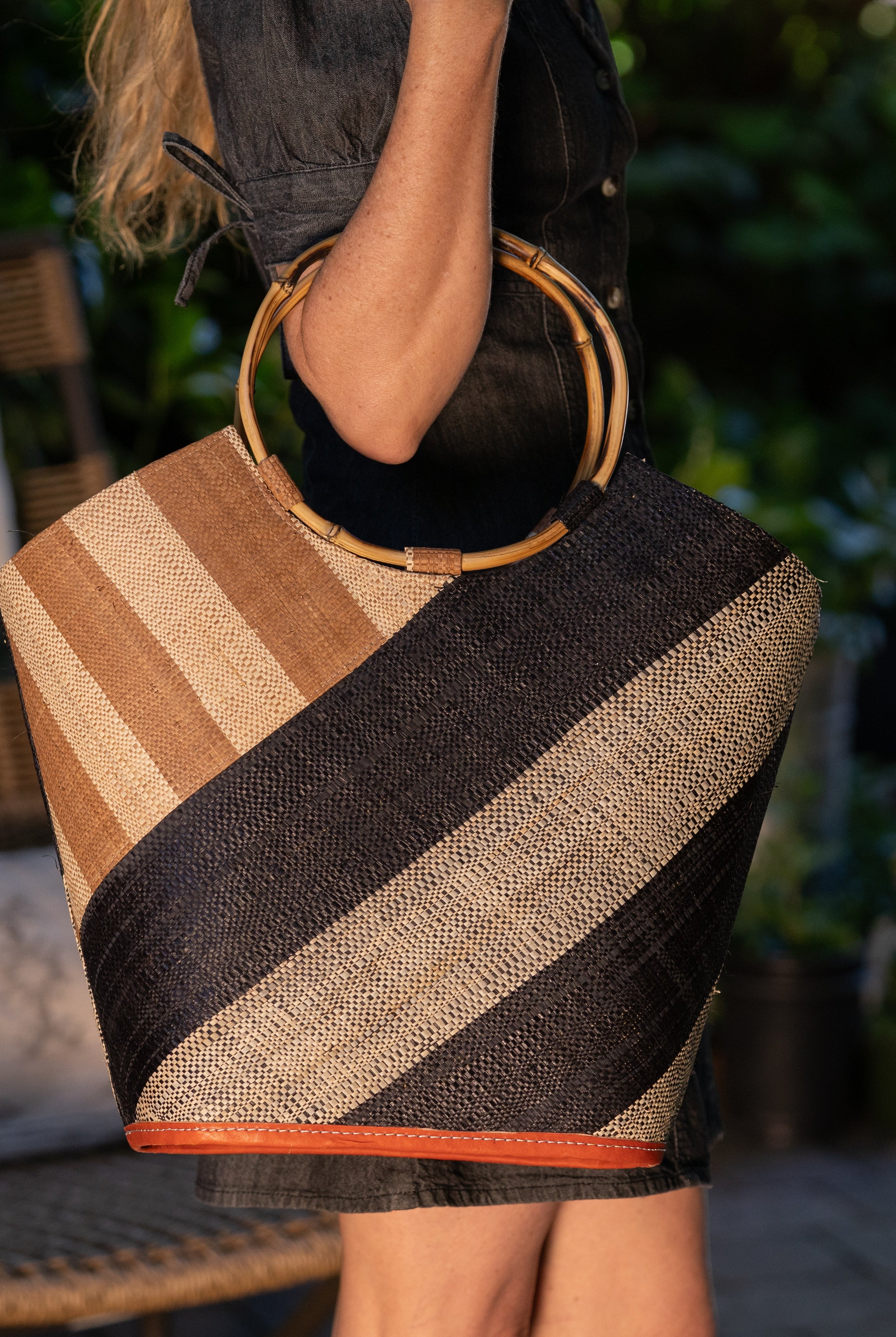 Model wearing Carmen Double Wide Stripe Black & Cappuccino Straw Bucket Bag w/ Bamboo Handle handmade loomed raffia palm fiber in even width wide stripe pattern of black and natural straw color oriented on the diagonal of three quarters of the bag with matching stripe pattern of cappuccino tea/light/brown and natural diagonally on the top left corner quarter shoulder bag handbag - Shebobo