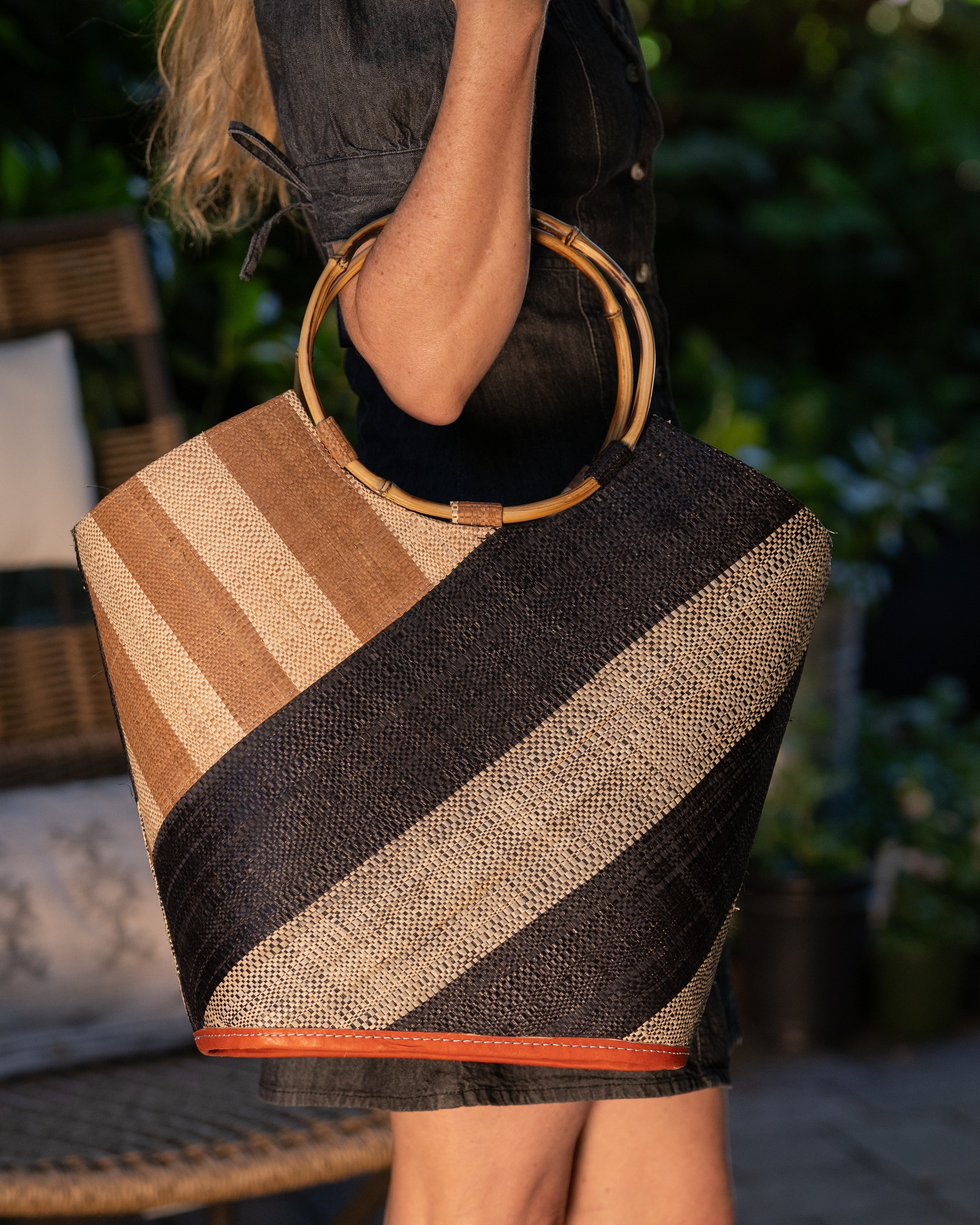 Model wearing Carmen Double Wide Stripe Black & Cappuccino Straw Bucket Bag w/ Bamboo Handle handmade loomed raffia palm fiber in even width wide stripe pattern of black and natural straw color oriented on the diagonal of three quarters of the bag with matching stripe pattern of cappuccino tea/light/brown and natural diagonally on the top left corner quarter shoulder bag handbag - Shebobo