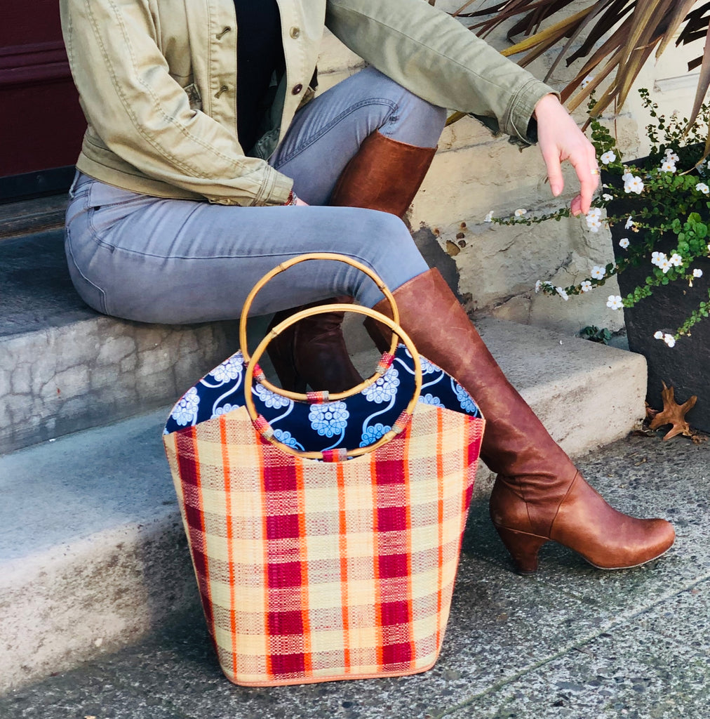 Model wearing Carmen Straw Bucket Bag with Bamboo Handles Bordeaux Multi Gingham handmade loomed raffia in a plaid pattern of natural straw color, coral orange/red, grey, and bordeaux/dark wine red/purple with assorted liners of African print fabric purse handbag - Shebobo
