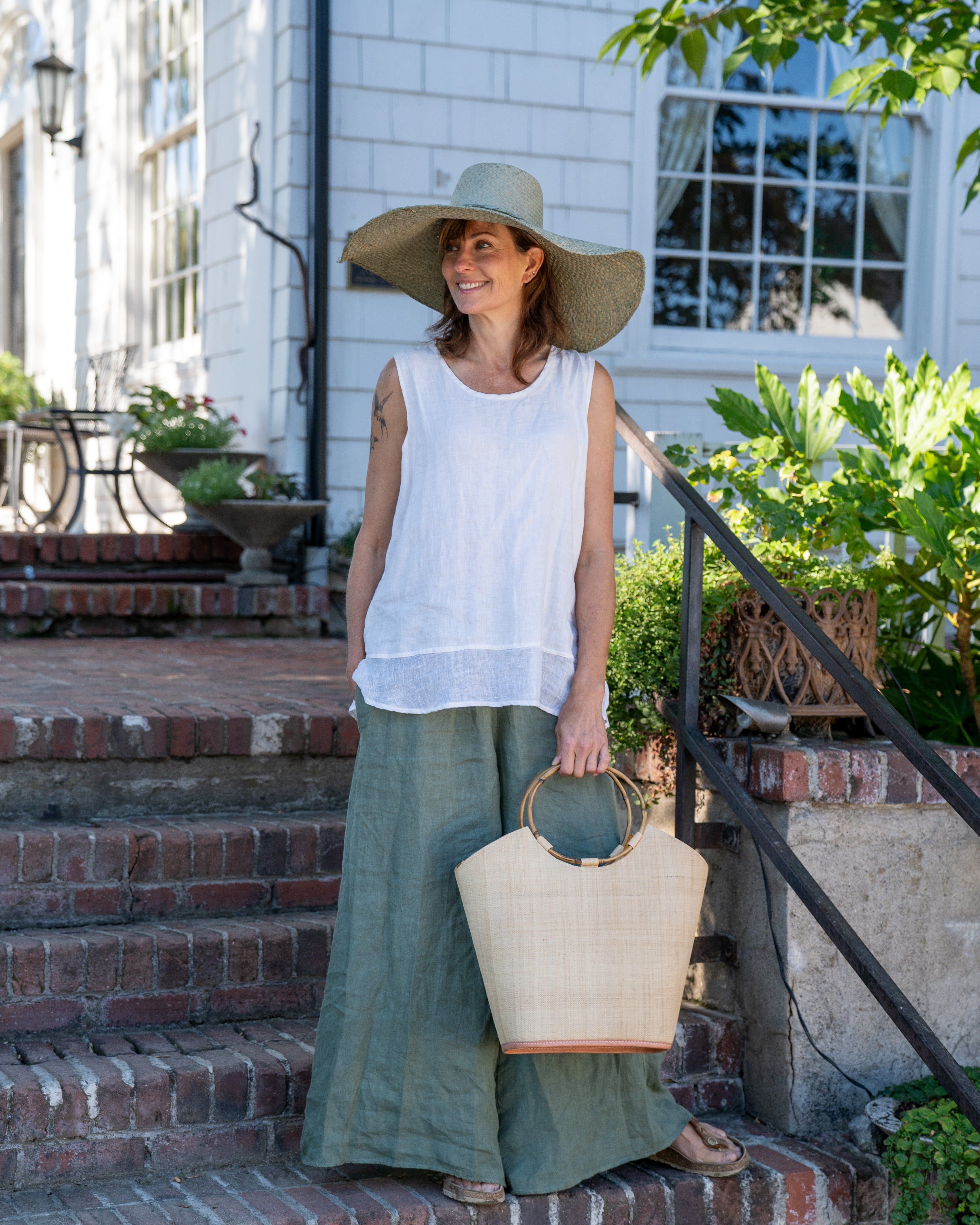 Model wearing Carmen Natural Straw Bucket Bag with Bamboo Handles handmade loomed raffia in a solid hue of natural straw color with assorted African print fabric liner handbag - Shebobo (with Natasha 7" Wide Brim Woven XL Straw Sun Hats)