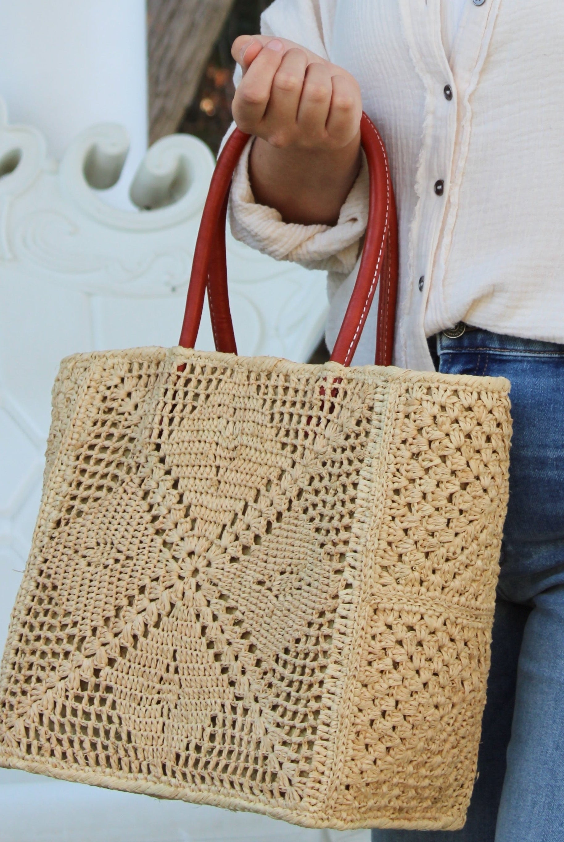 Model wearing Cheval Lace Square Pattern Crochet Straw Basket Bag handmade from natural raffia palm fiber in a lace square geometric diamond pattern with triangle detailing textile in a natural straw color with leather handles handbag purse beach bag tote- Shebobo