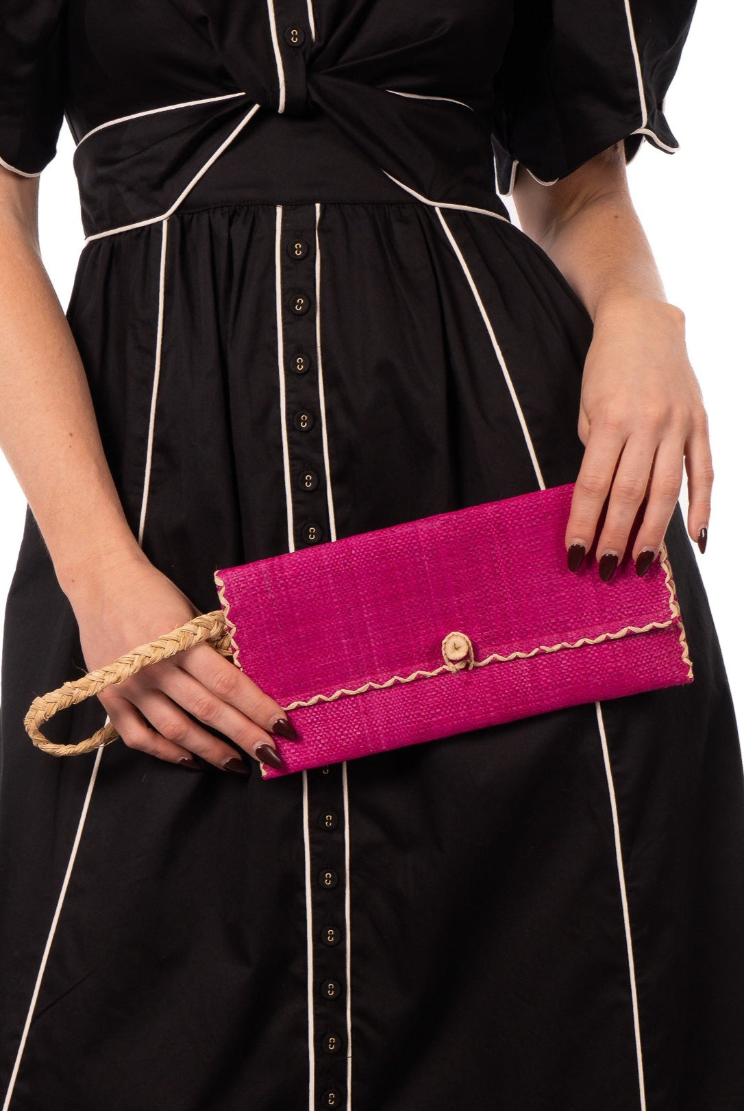 Model wearing ChiChi Fuchsia Straw Clutch Bag handmade loomed raffia palm fiber wristlet in fuchsia hot/bright/barbie/pink color with natural straw color cross stitch edging, button & loop closure, and braided wrist strap - Shebobo
