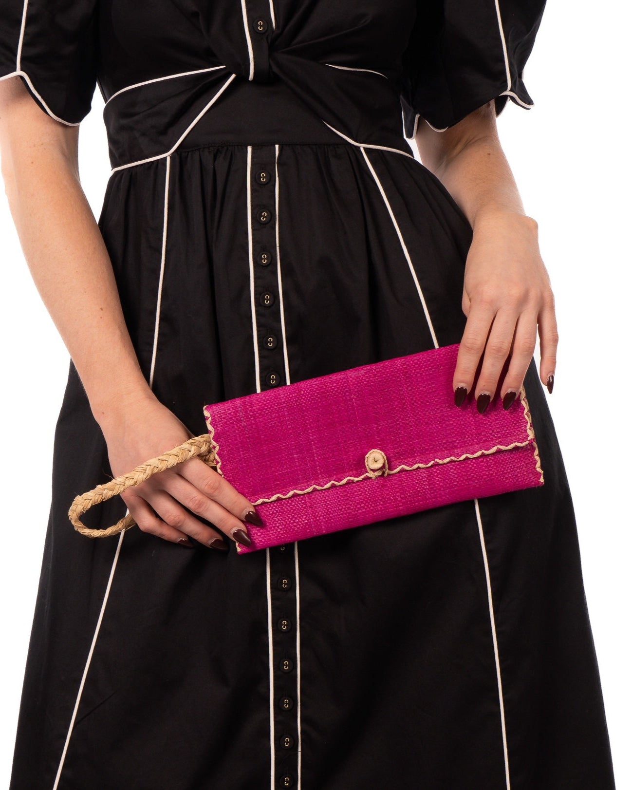 Model wearing ChiChi Fuchsia Straw Clutch Bag handmade loomed raffia palm fiber wristlet in fuchsia hot/bright/barbie/pink color with natural straw color cross stitch edging, button & loop closure, and braided wrist strap - Shebobo