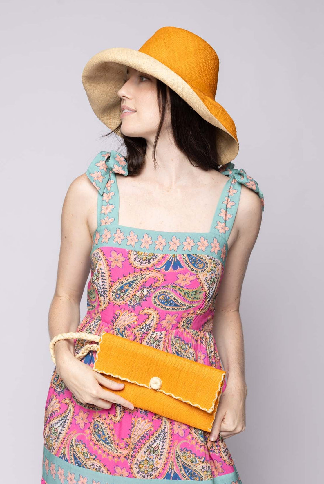 Model wearing ChiChi Saffron Straw Clutch Bag handmade loomed raffia palm fiber wristlet in saffron yellow/orange color with natural straw color cross stitch edging, button & loop closure, and braided wrist strap - Shebobo