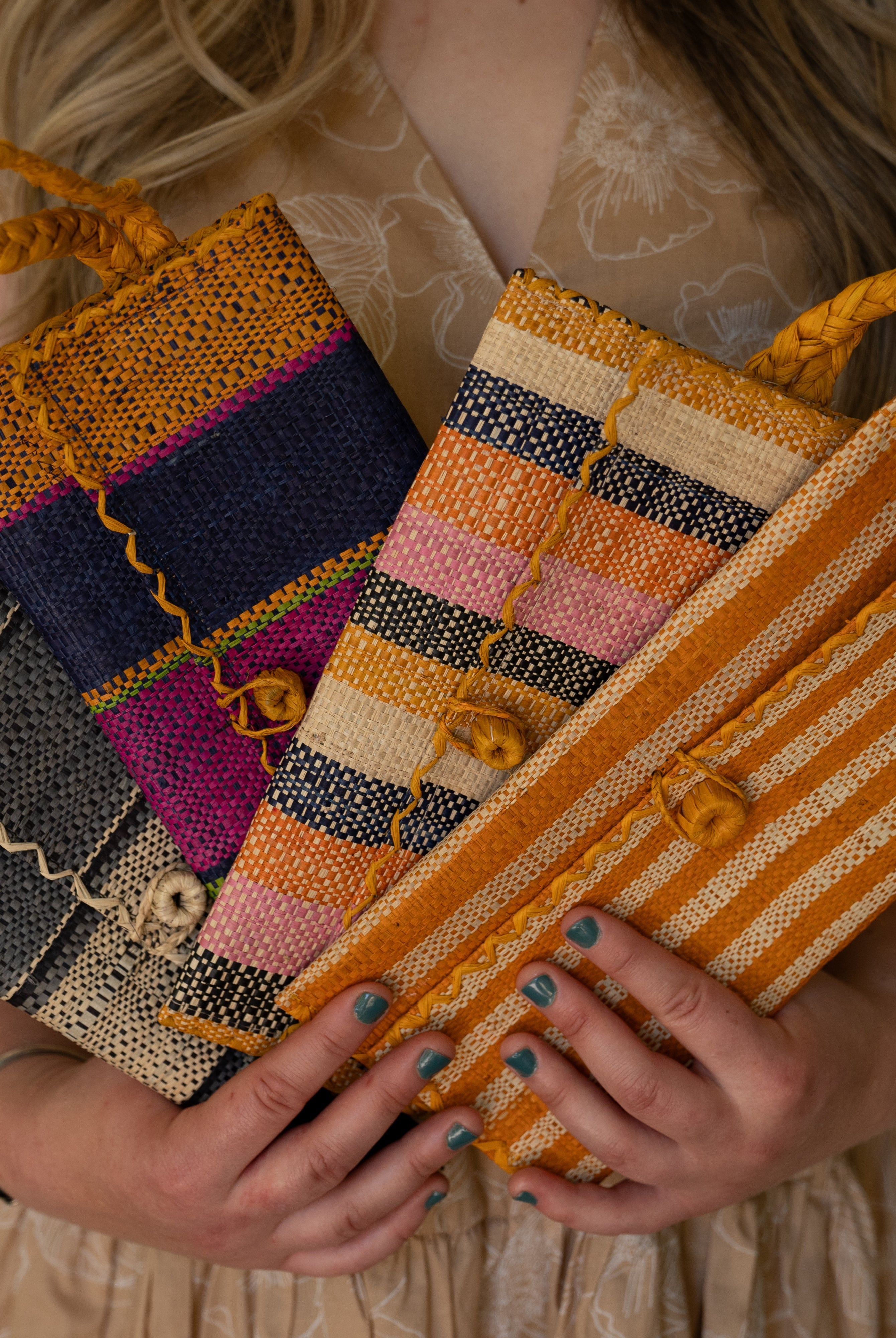 Model wearing multiple solid hues of ChiChi Straw Clutch Wristlet Bag handmade loomed raffia palm fiber in vibrant colors with natural cross stitch edging and raffia loop button closure with matching braided wrist loop with 4" Brim Genevieve Crochet Straw Sun Hats with Lace Weave Edge in Natural Raffia - Shebobo