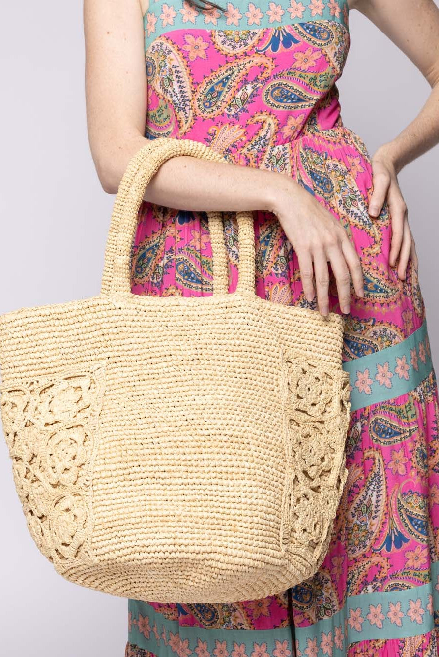 Model wearing Colette FlowerCrochet Straw Basket Handbag with Pockets handmade natural raffia palm fiber in a solid hue of natural straw color with geometric granny square floral cutout pattern on two large external pockets tote bag - Shebobo