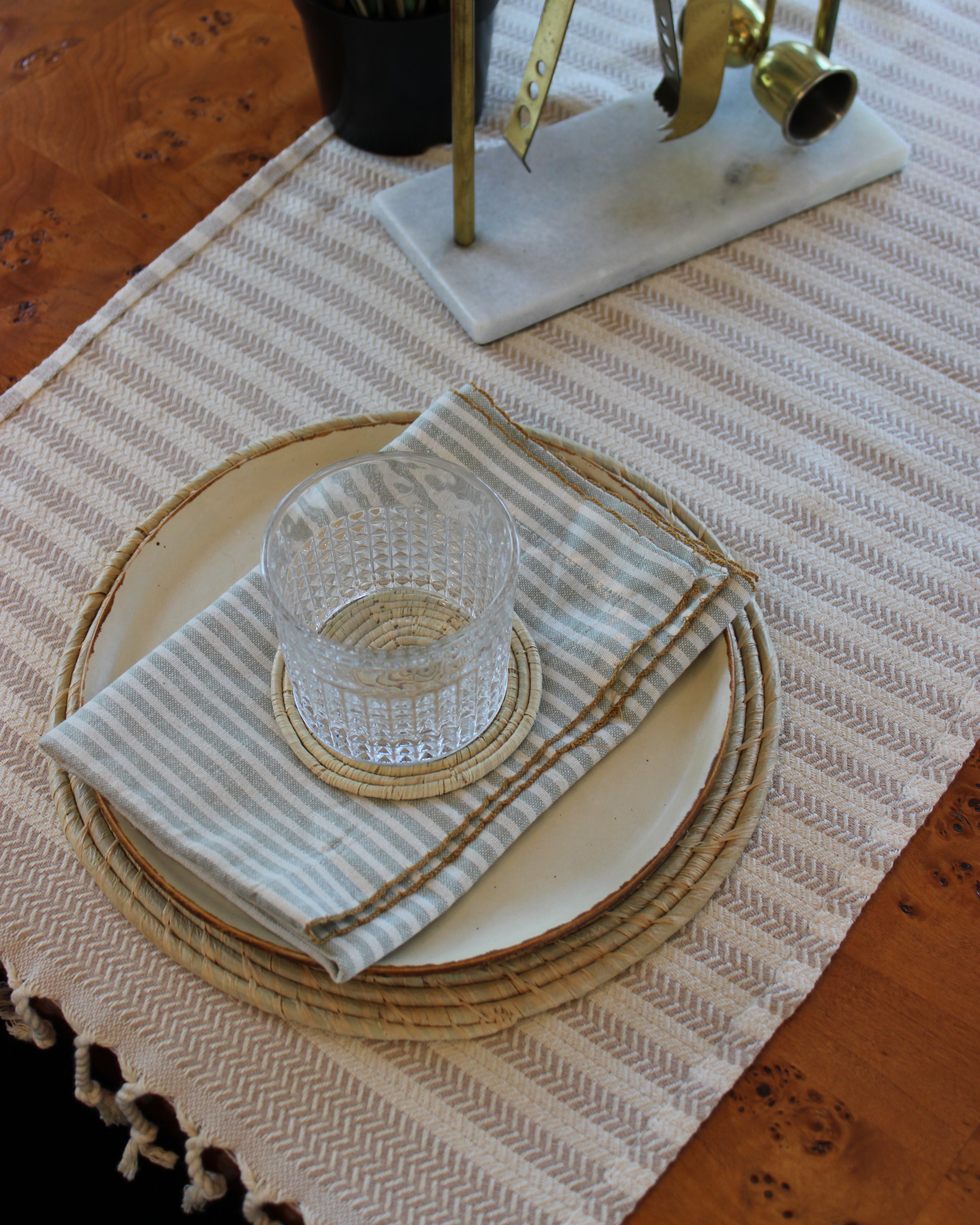 Lifestyle view Dabu Round Two Tone Swirl Raffia Straw Coasters & Placemats Set of 6 handmade natural raffia palm fiber in a crochet loop disc technique creating concentric circular stripe pattern of texture in a solid hue of natural straw color with matching knotted spiral swirl weave sets of six placemats or coasters - Shebobo