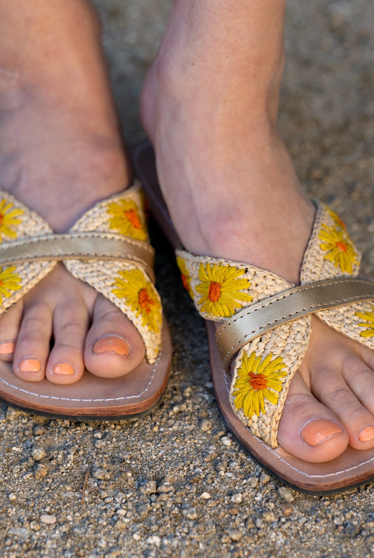 Model wearing Daisy Crochet Straw & Leather Sandal with Flower Embroidery & Metallic Detailing handmade crochet natural raffia palm fiber in a solid hue of natural straw color in two bands with saffron yellow petals and coral orange/red centered embroidered flower pattern wrap around the top of the shoe with a band of metallic gold across the top summer sandals shoes - Shebobo