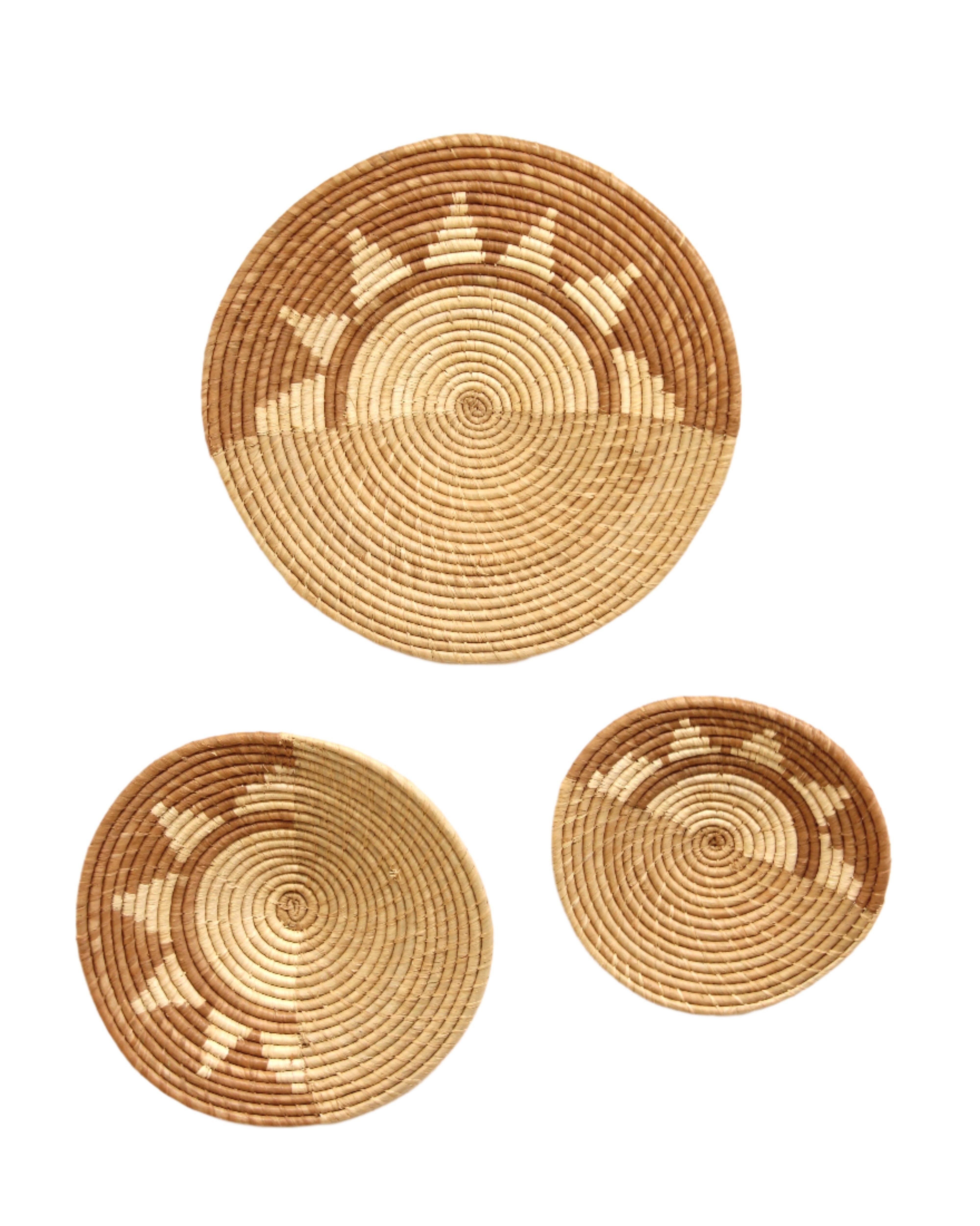 Dakarai Raffia Straw Wall Decor Display Basket Trays: Set of 3 handmade woven raffia palm fiber in a crochet loop technique creating a concentric swirl pattern of bands of cinnamon/tobacco/brown, cappuccino/tea/light brown, and natural straw color that create a two tone pattern with half of the disc being light brown, and the other half a sun burst pattern set of three sized flat bowl trays - Shebobo