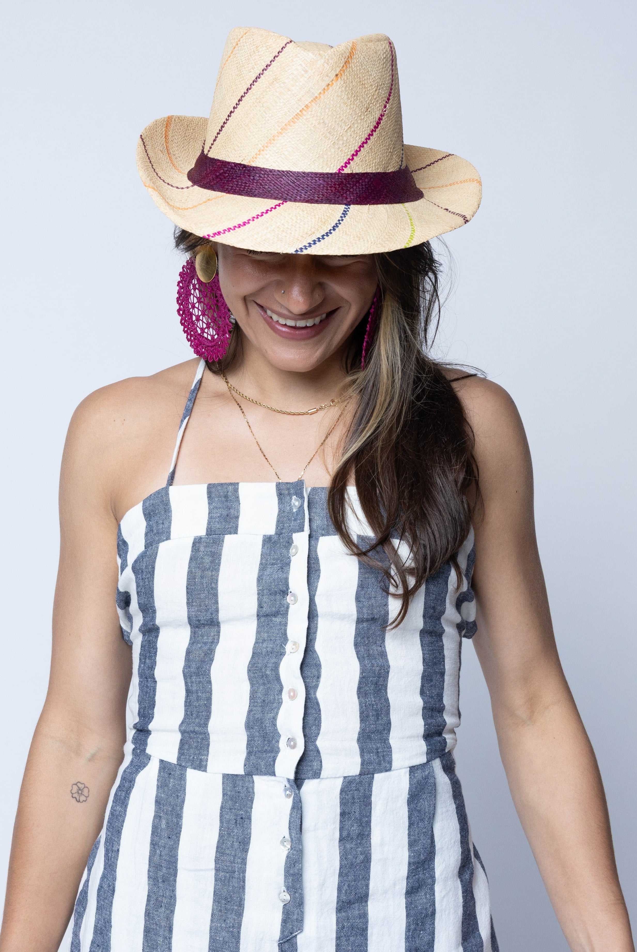 Model wearing Fedra 2" Brim Fedora Unisex Straw Hats natural and brights multicolor pinstripes packable raffia straw hat handmade loomed raffia in wide bands of natural straw color with narrow bands of lime green, bordeaux red, fuchsia pink, orange, cinnaon/tobacco/brown, blush orange/pink, etc. create a stripe swirl pattern - Shebobo