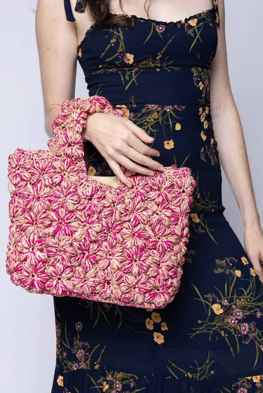 Model wearing Florence Fuchsia Pinks Multicolor Flower Crochet Straw Basket Handbag handmade natural raffia palm fiber in a multicolor hue combination of natural straw color, fuchsia hot/bright/pink, and light pink with subtle tied flower design consisting of 88 flowers crochet together along the outside of the bag as well as the handles purse tote - Shebobo