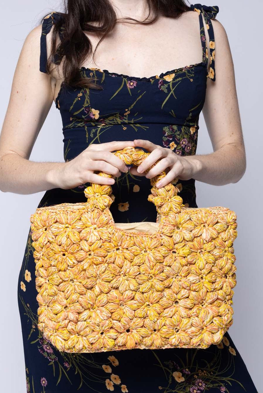 Model wearing Florence Lemon Yellows Multicolor Flower Crochet Straw Basket Handbag handmade natural raffia palm fiber in a multicolor hue combination of natural straw color, lemon yellow, and orange with subtle tied flower design consisting of 88 flowers crochet together along the outside of the bag as well as the handles purse tote - Shebobo