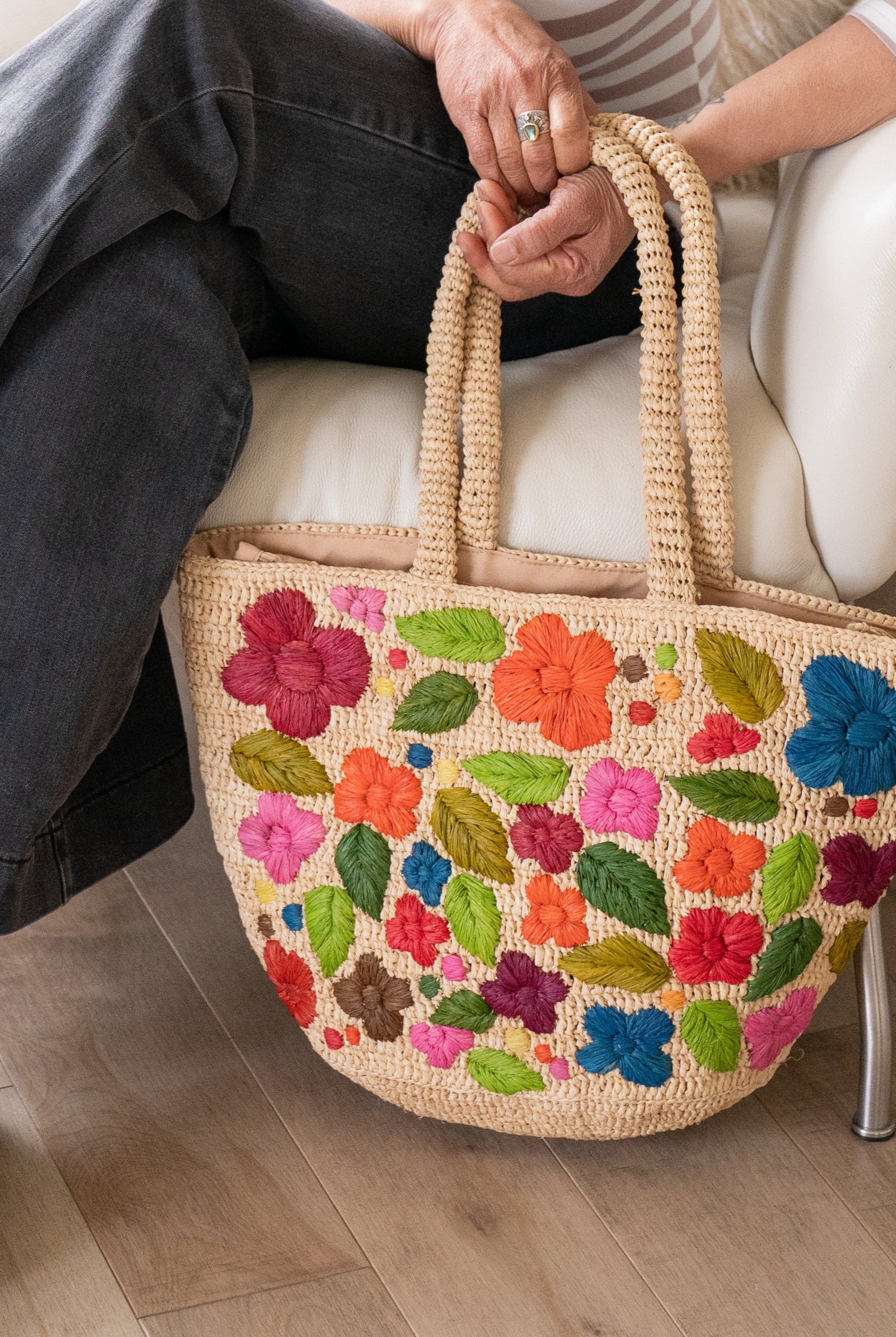 Model wearing Full Bloom Crochet Straw Handbag with Embroidered Flowers handmade natural raffia palm fiber in a solid hue of natural straw color with subtle horizontal banded link texture and multicolor embroidered detailing in fuchsia hot/bright/barbie/pink, light pink, red, coral orange/red, orange, dark chocolate brown, cinnamon/tobacco/dark/brown, dusk navy/dark/blue, green, olive green, lime green, yellow, purple, etc. colored flowers, leaves and dots embellishment tote beach bag purse - Shebobo
