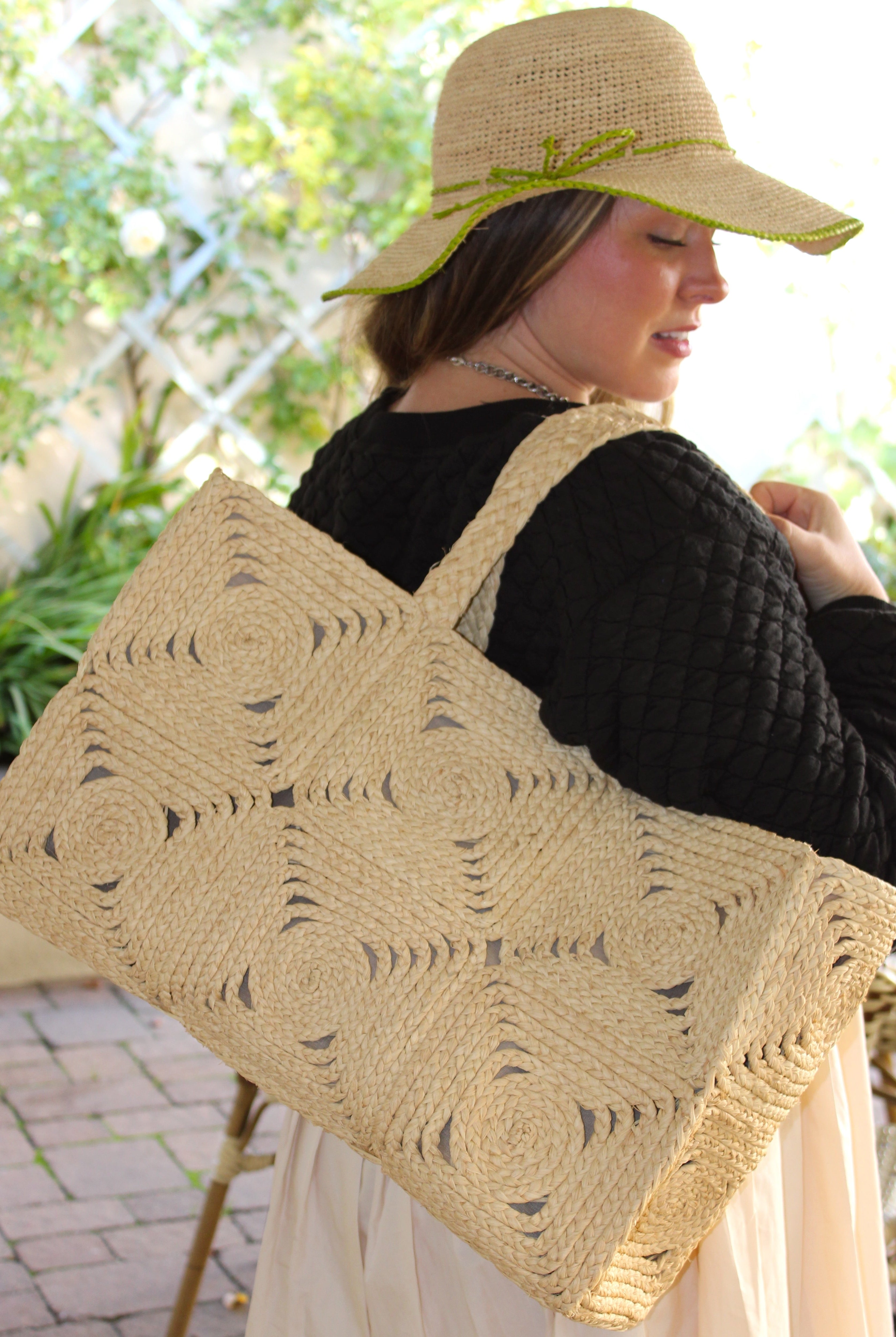 Model wearing Gemma Crochet Disc Rectangle Large Straw Basket Handbag handmade braided natural raffia palm fiber in a solid hue of Natural straw color with subtle square disc pattern around the outside of the bag in two horizontal bands of squares creating a geometric pattern and matching woven handles beach bag purse - Shebobo (with Rachel 4" Brim Crochet Straw Sun Hats with Colored Edge)