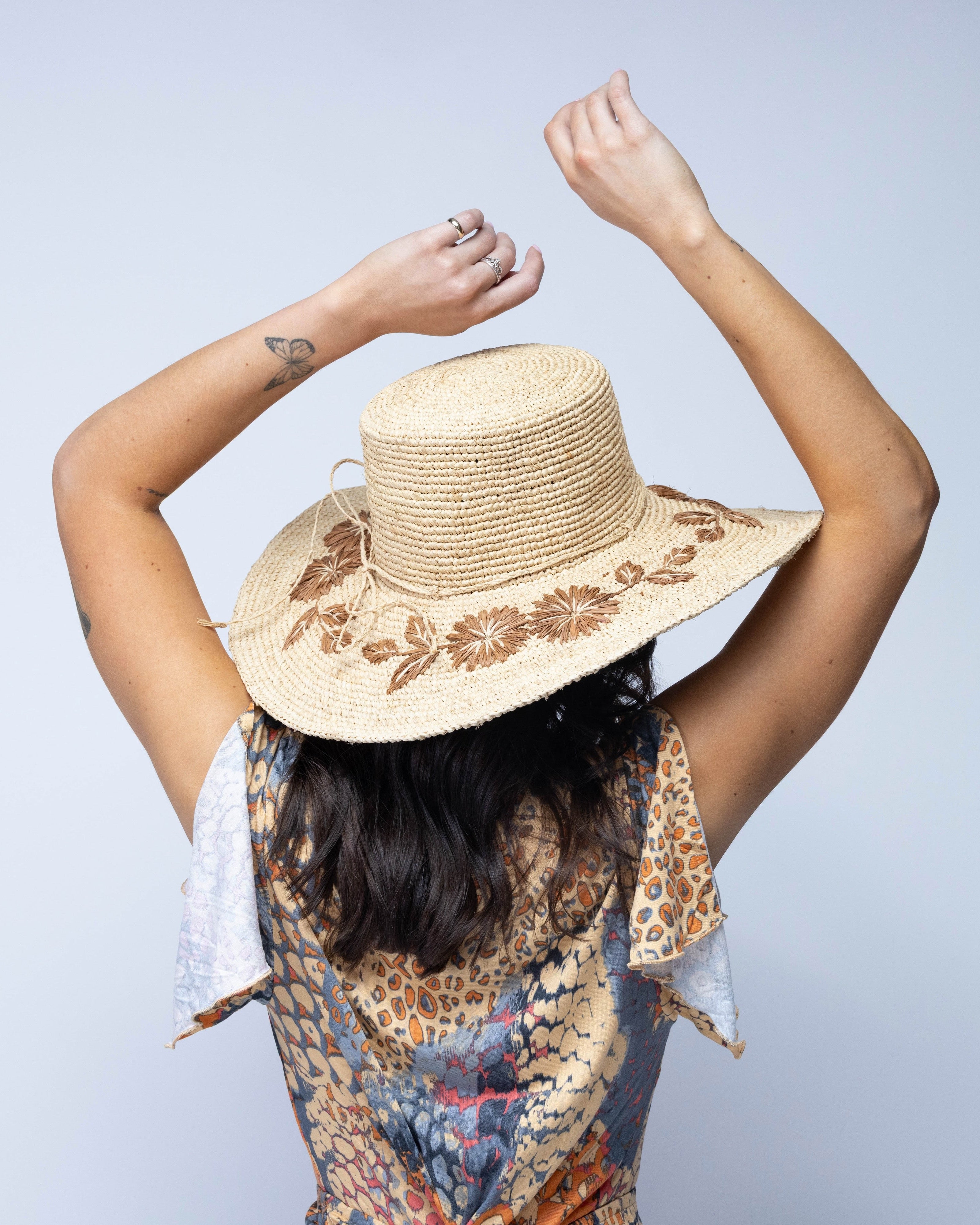 Model wearing 5.5" Brim Gigi Natural and Cinnamon Floral Embroidered Crochet Straw Sun Hats handmade crochet natural raffia palm fiber in a solid hue of natural straw color making a concentric pattern from the center top of the flattened crown spiraling out to the edge of the brim with matching adjustable raffia braid hat band and cinnamon dark brown floral pattern with leaves embroidered on the brim - Shebobo
