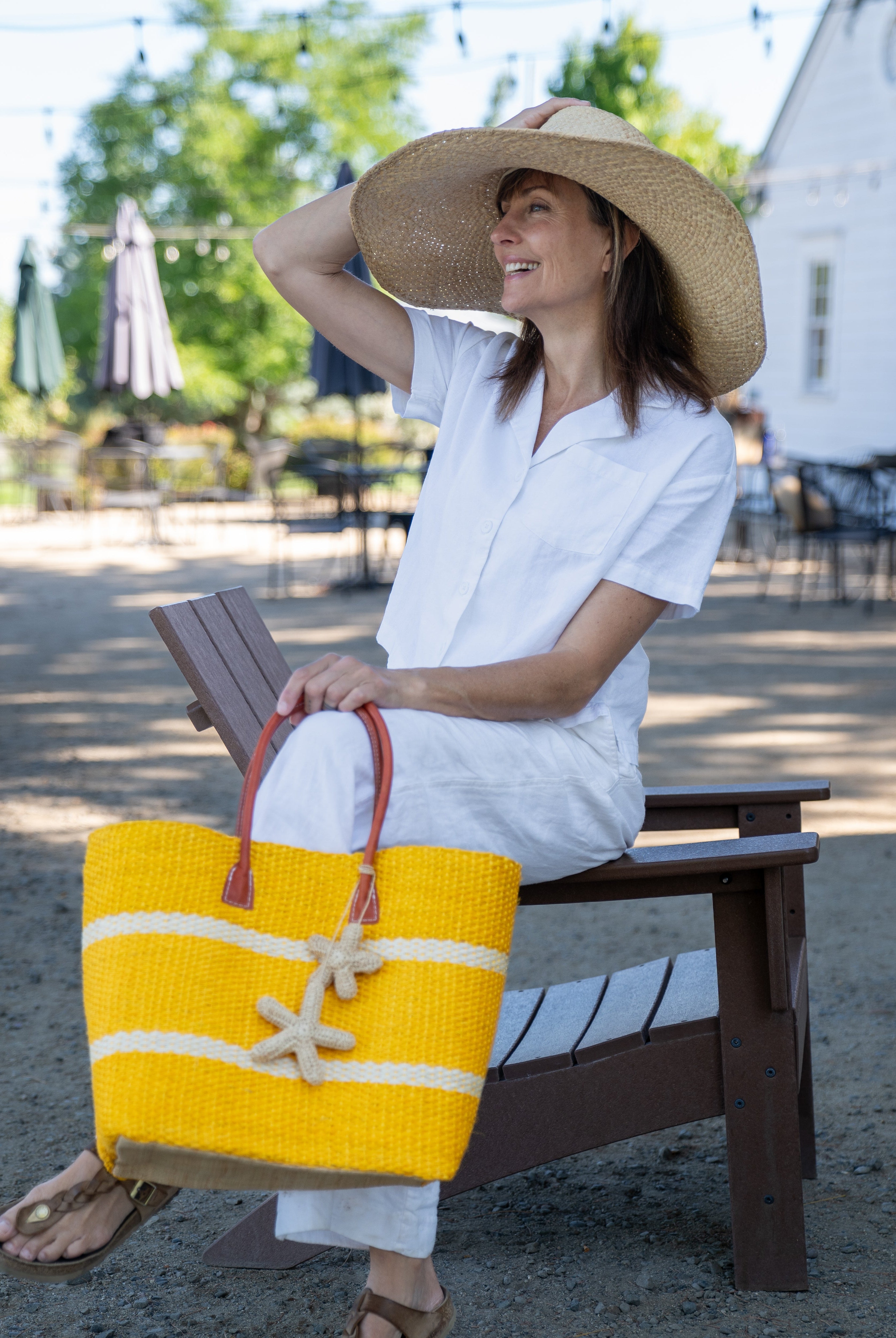 Model wearing Havana Sisal Basket Bag with Tassel Charm Embellishment handmade sisal fiber woven into horizontal wide bands of saffron yellow with two evenly spaced narrow bands of natural straw color create a stripe pattern with natural crochet starfish charm embellishment and leather handles handbag shoulder bag - Shebobo (with Natasha 7" Wide Brim Woven XL Straw Sun Hats)