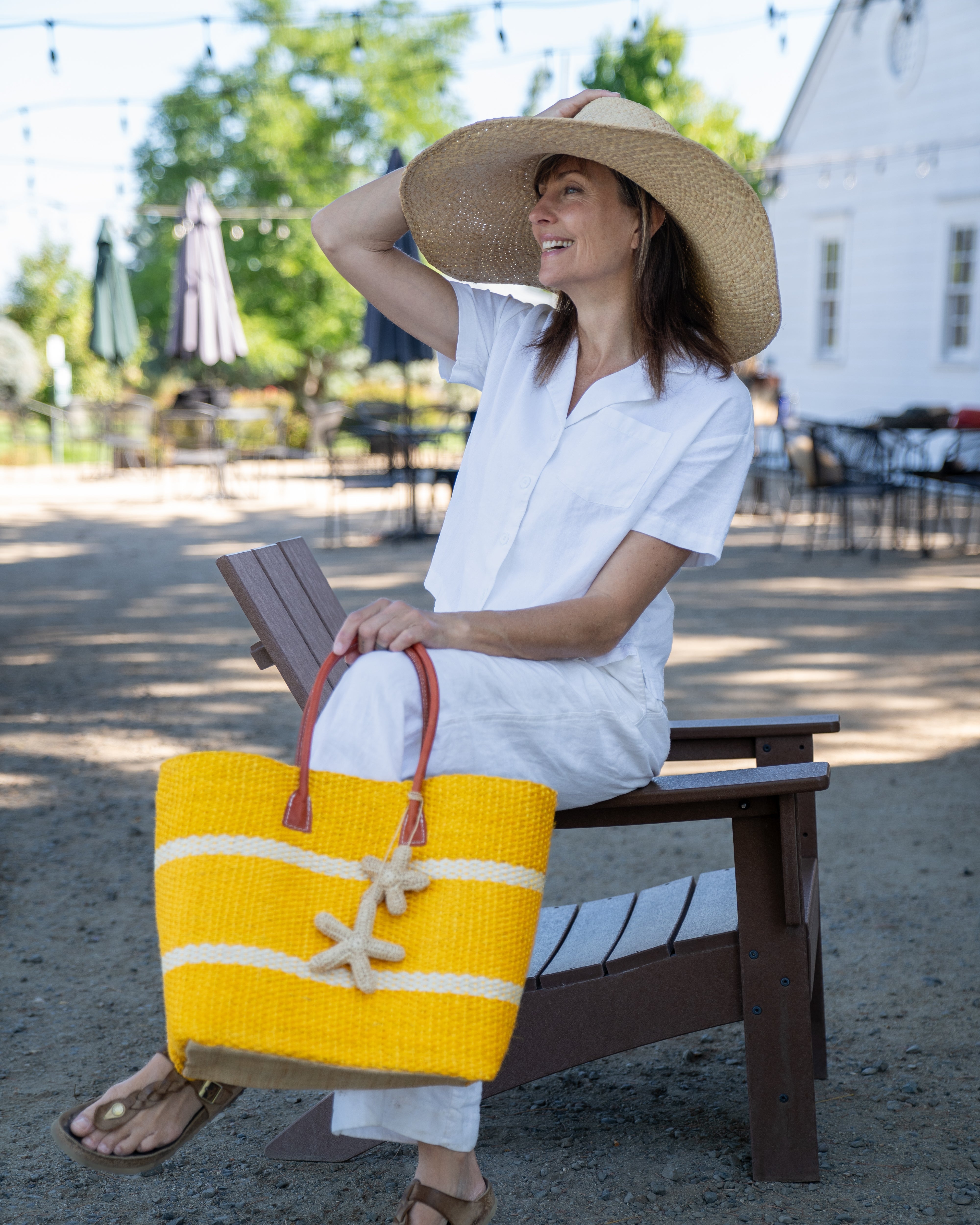 Model wearing Havana Sisal Basket Bag with Tassel Charm Embellishment handmade sisal fiber woven into horizontal wide bands of saffron yellow with two evenly spaced narrow bands of natural straw color create a stripe pattern with natural crochet starfish charm embellishment and leather handles handbag shoulder bag - Shebobo (with Natasha 7" Wide Brim Woven XL Straw Sun Hats)