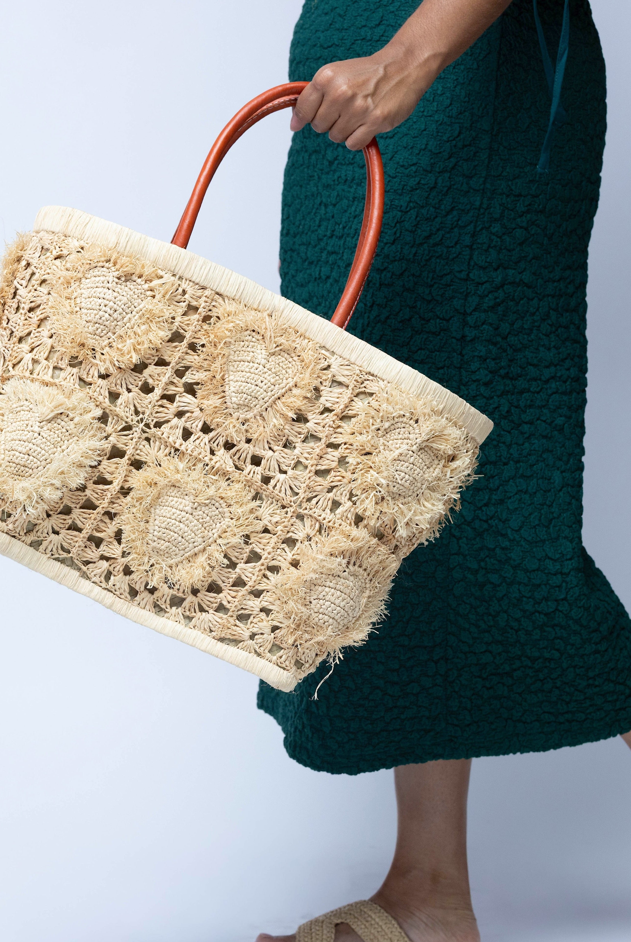 Model wearing Hearts Crochet Straw Basket Bag with Fringed Heart Pattern handmade woven raffia in a solid hue of natural straw color with granny square pattern and raised/stuffed heart pattern with fringe edges on each heart, looped base and top binding, as well as leather handles purse beach bag shoulder bag - Shebobo