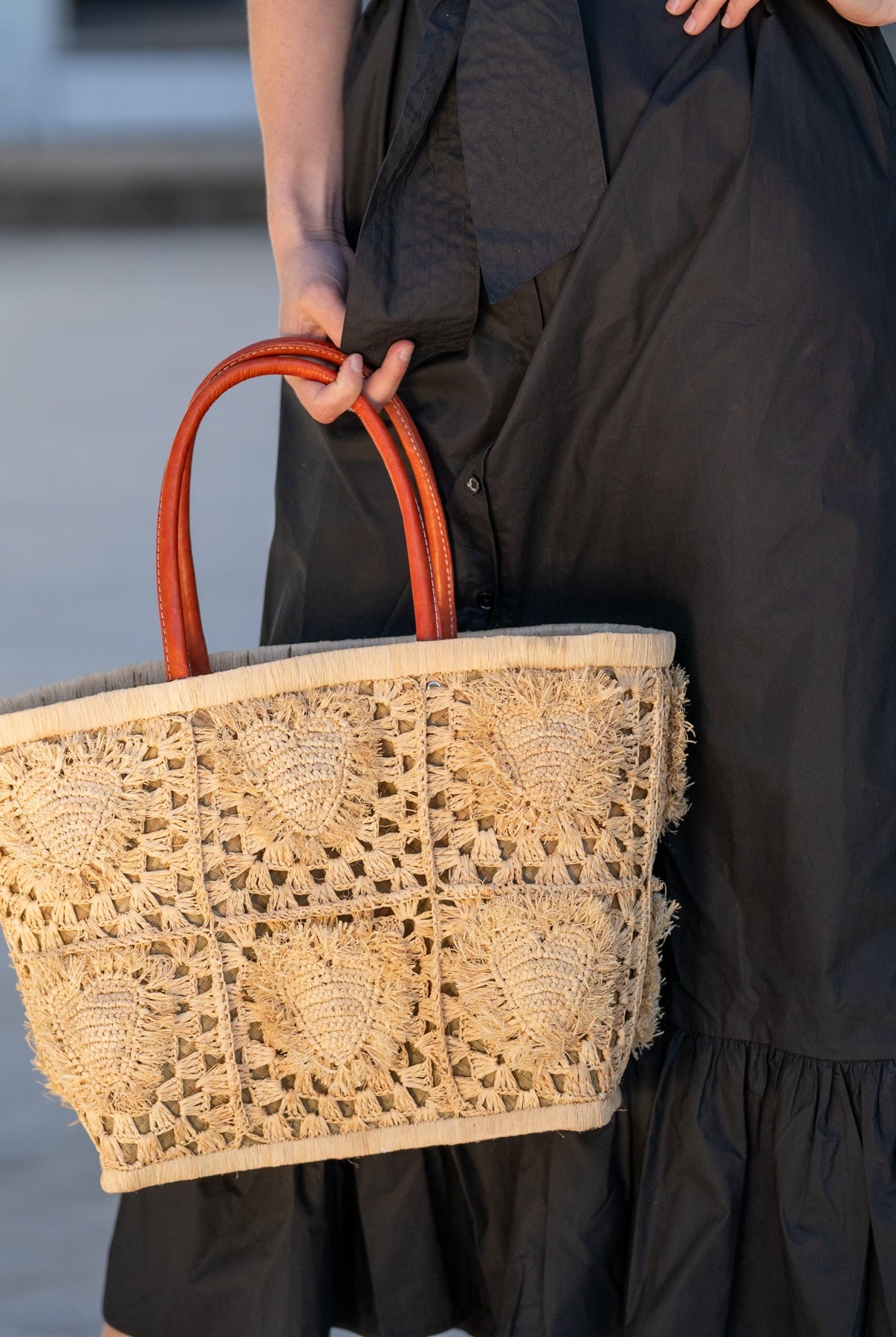 Model wearing Hearts Crochet Straw Basket Bag with Fringed Heart Pattern handmade woven raffia in a solid hue of natural straw color with granny square pattern and raised/stuffed heart pattern with fringe edges on each heart, looped base and top binding, as well as leather handles purse beach bag shoulder bag - Shebobo