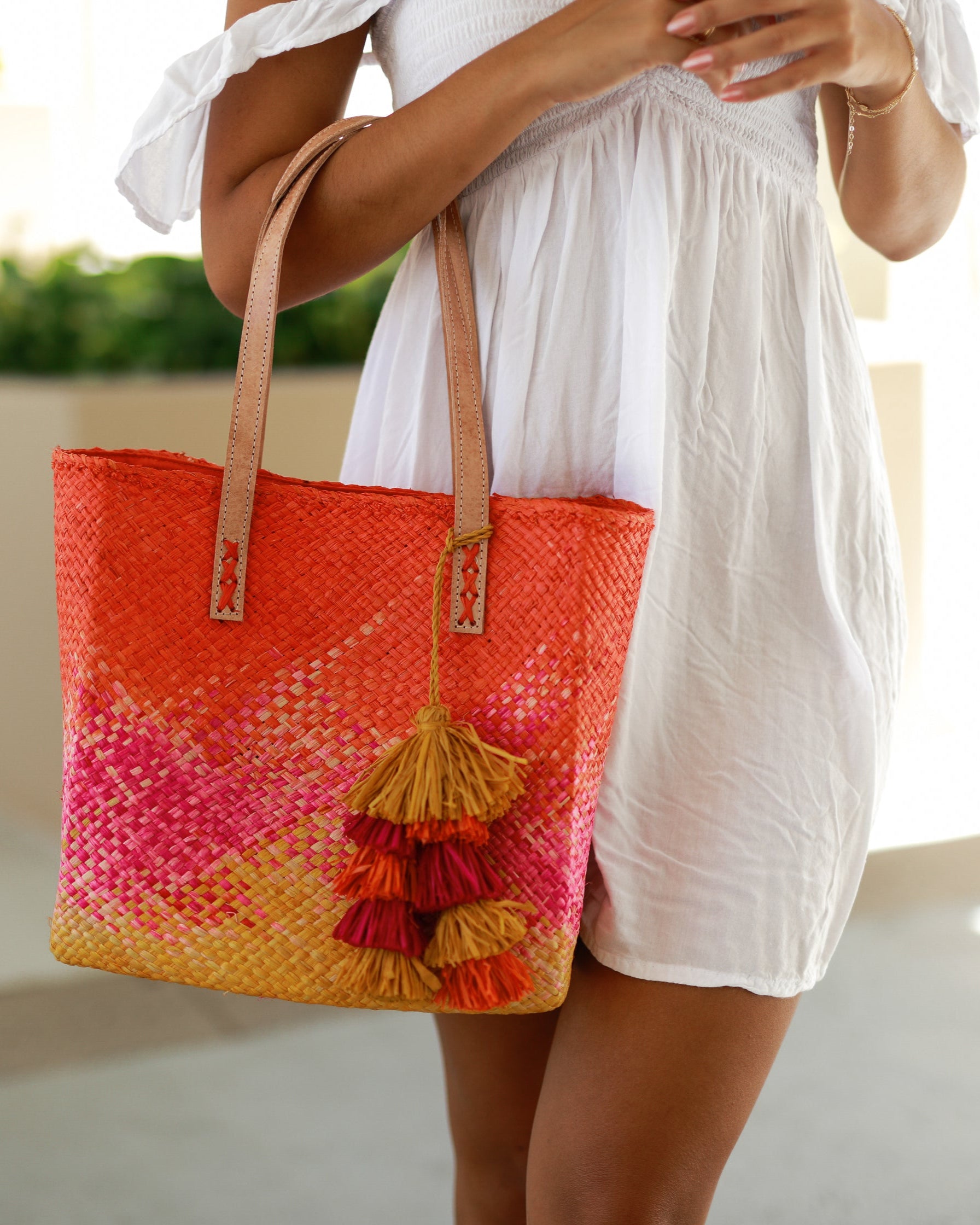 Model wearing Holden Ombre Fuchsia Straw Handbag Tassel Charm Embellishment handmade woven raffia dip dyed gradient of coral orange/red, fuchsia bright pink, and saffron yellow with matching multicolored, multi-tiered raffia tuft tassel - Shebobo