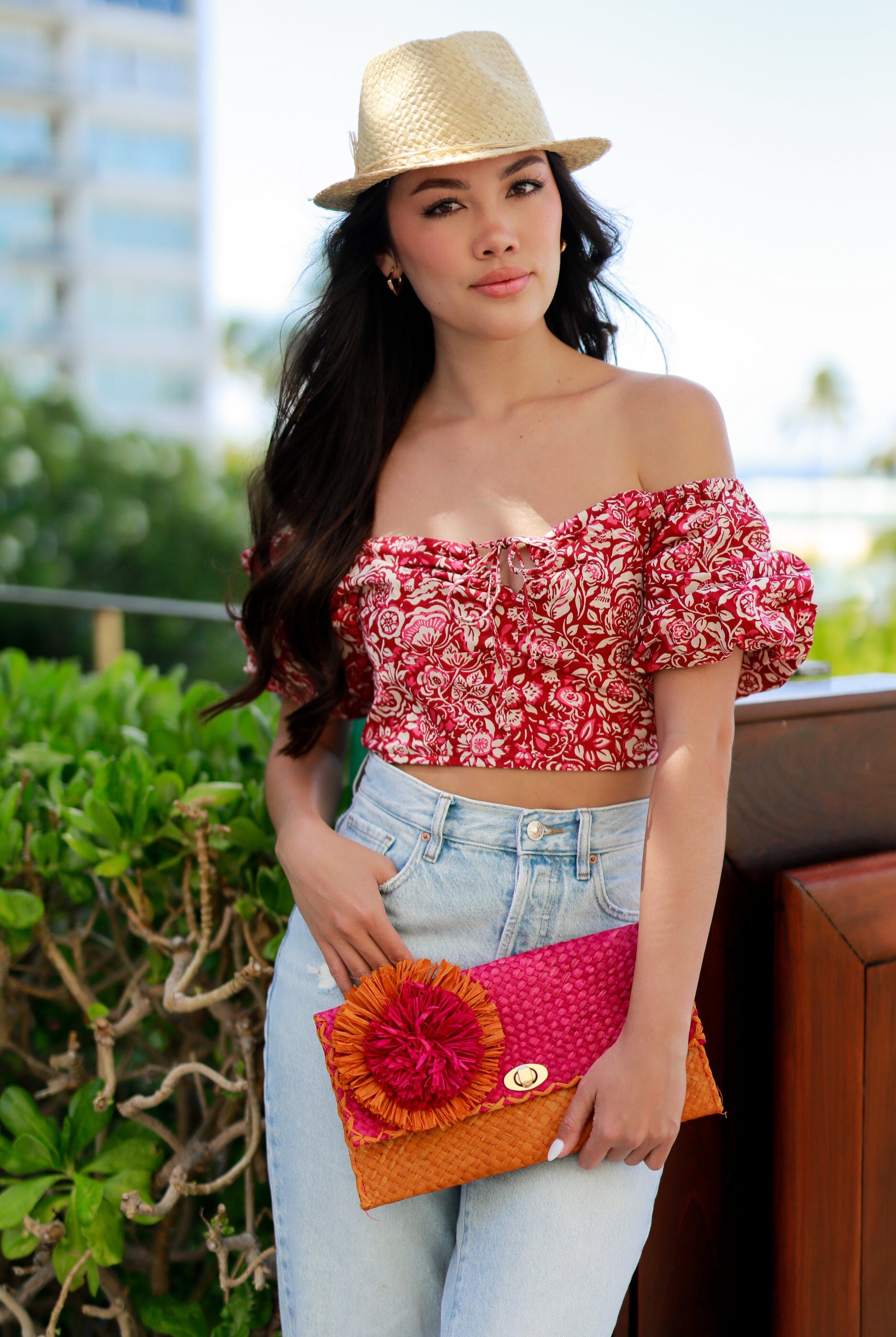 Model wearing Holden Ombre Fuchsia Straw Clutch with Flower Pouf handmade woven raffia dip dyed gradient of fuchsia bright/barbie/pink, saffron yellow, and coral orange/red with large coral and fuchsia fringe flower embellishment - Shebobo (with Charlie Natural Unisex Fedora Straw Hat)
