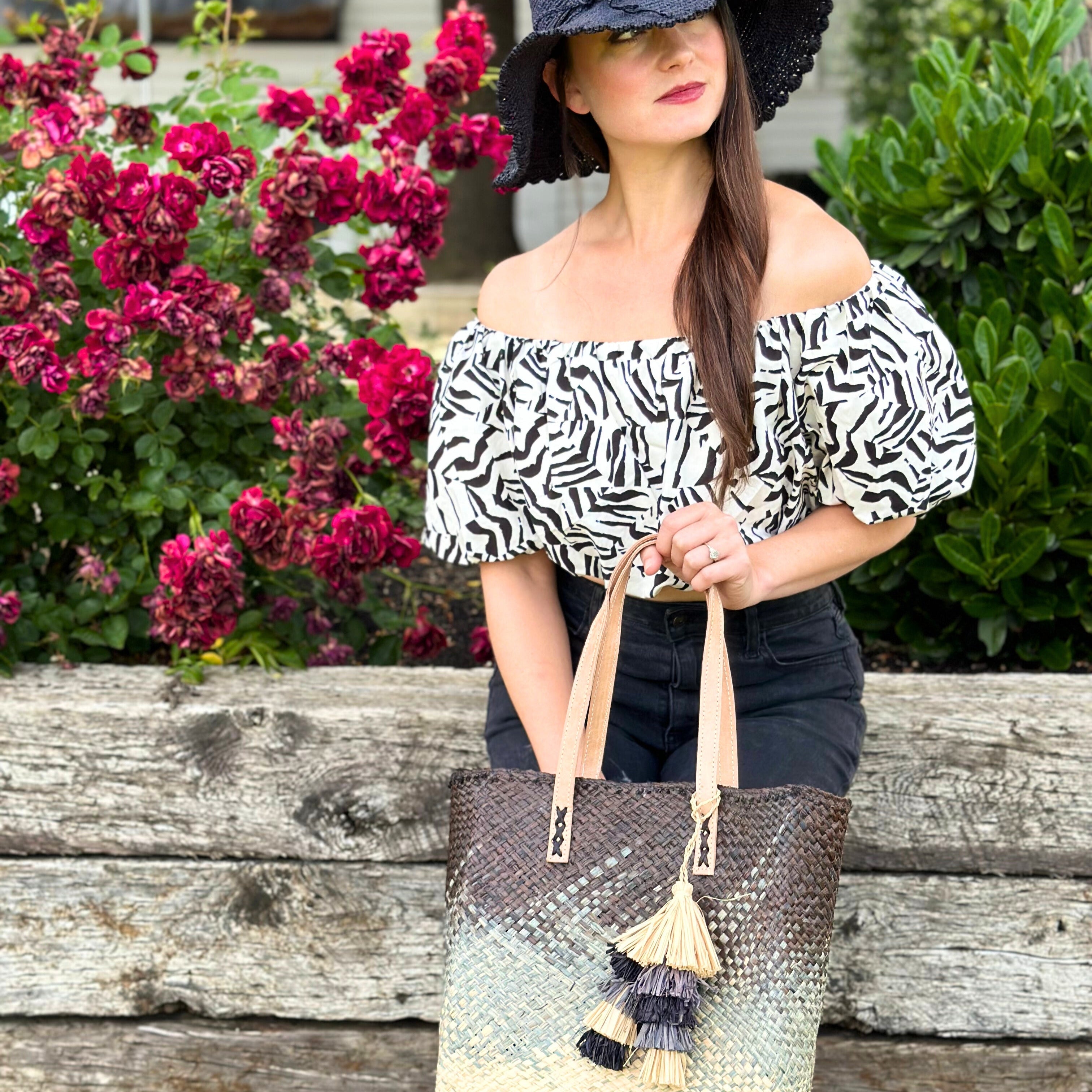 Model wearing Holden Ombre Black Straw Handbag Tassel Charm Embellishment handmade woven raffia dip dyed gradient of black, grey, and natural with matching multicolored, multi-tiered raffia tuft tassel with 4" Brim Genevieve Crochet Straw Sun Hats with Lace Weave Edge Black - Shebobo