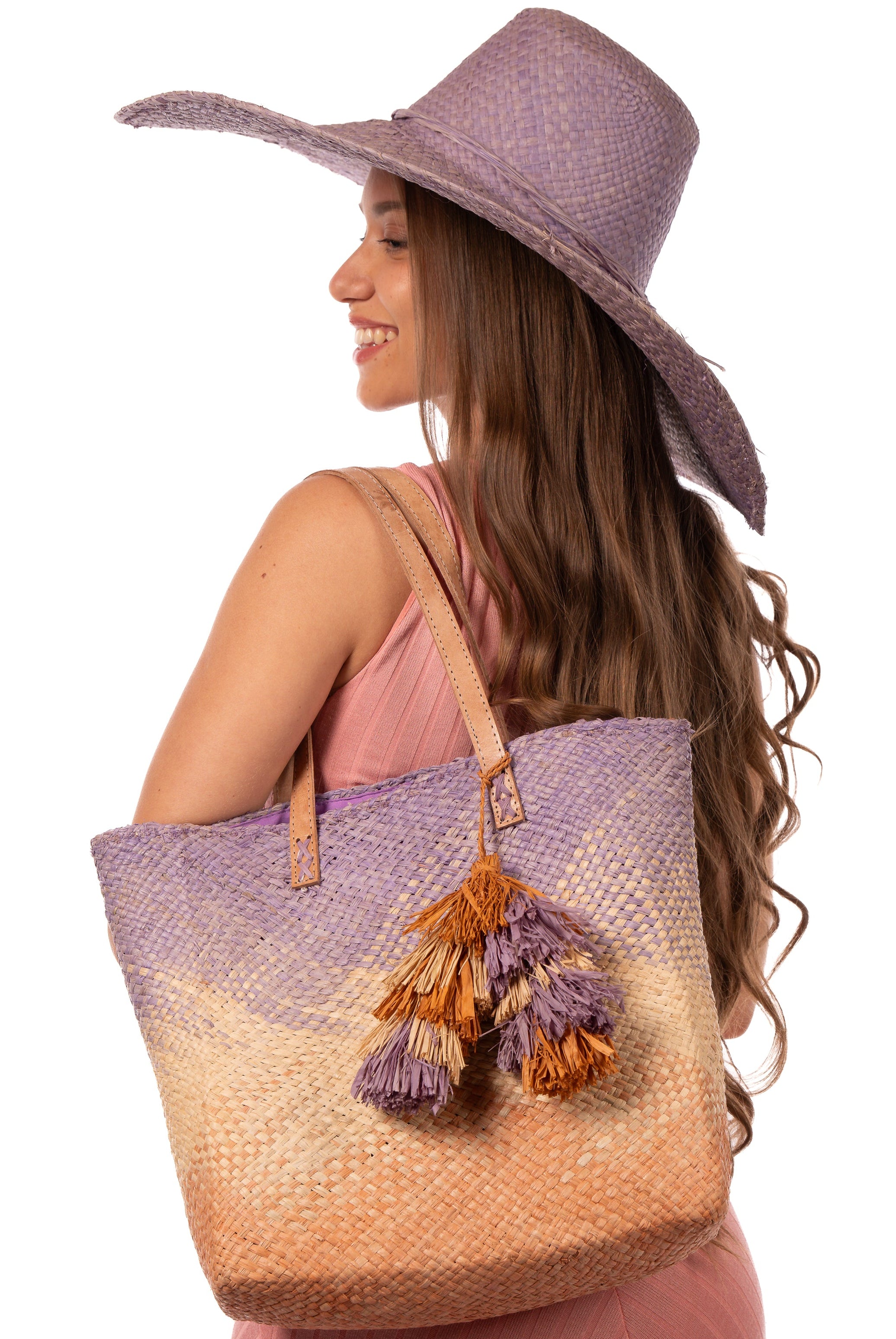Model wearing Holden Ombre Wisteria Straw Handbag Tassel Charm Embellishment handmade woven raffia dip dyed gradient of wisteria lavender/lilac/light/purple, natural straw color, and blush orange/pink with matching multicolored, multi-tiered raffia tuft tassel - Shebobo (with 7" Wide Brim Natasha Wisteria Woven Straw Sun Hat)