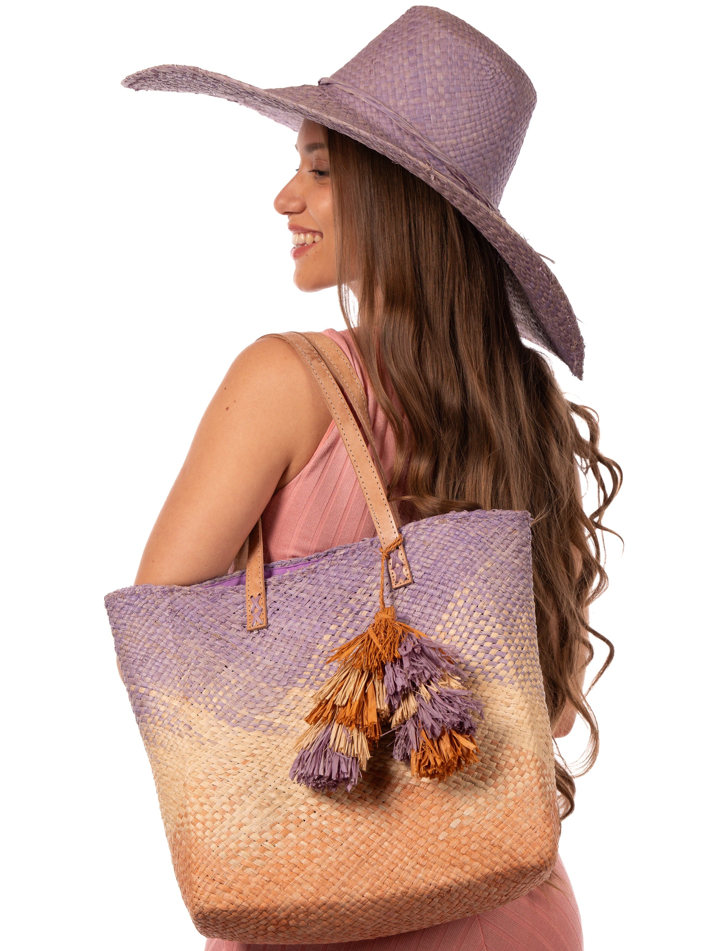 Model wearing Holden Ombre Wisteria Straw Handbag Tassel Charm Embellishment handmade woven raffia dip dyed gradient of wisteria lavender/lilac/light/purple, natural straw color, and blush orange/pink with matching multicolored, multi-tiered raffia tuft tassel - Shebobo (with 7" Wide Brim Natasha Wisteria Woven Straw Sun Hat)