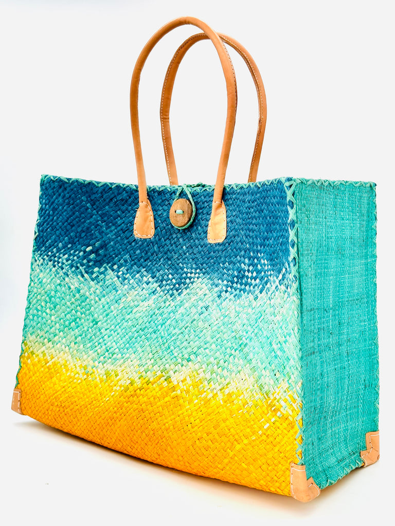 Side view Holden Turquoise Ombre Zafran Large Straw Beach Bags handmade dip dyed raffia woven into a three part horizontal ombre pattern of turquoise blue on the top, seafoam blue/green in the middle and both sides, and saffron yellow on the bottom with cross stitch edging, wooden button, and leather handles - Shebobo