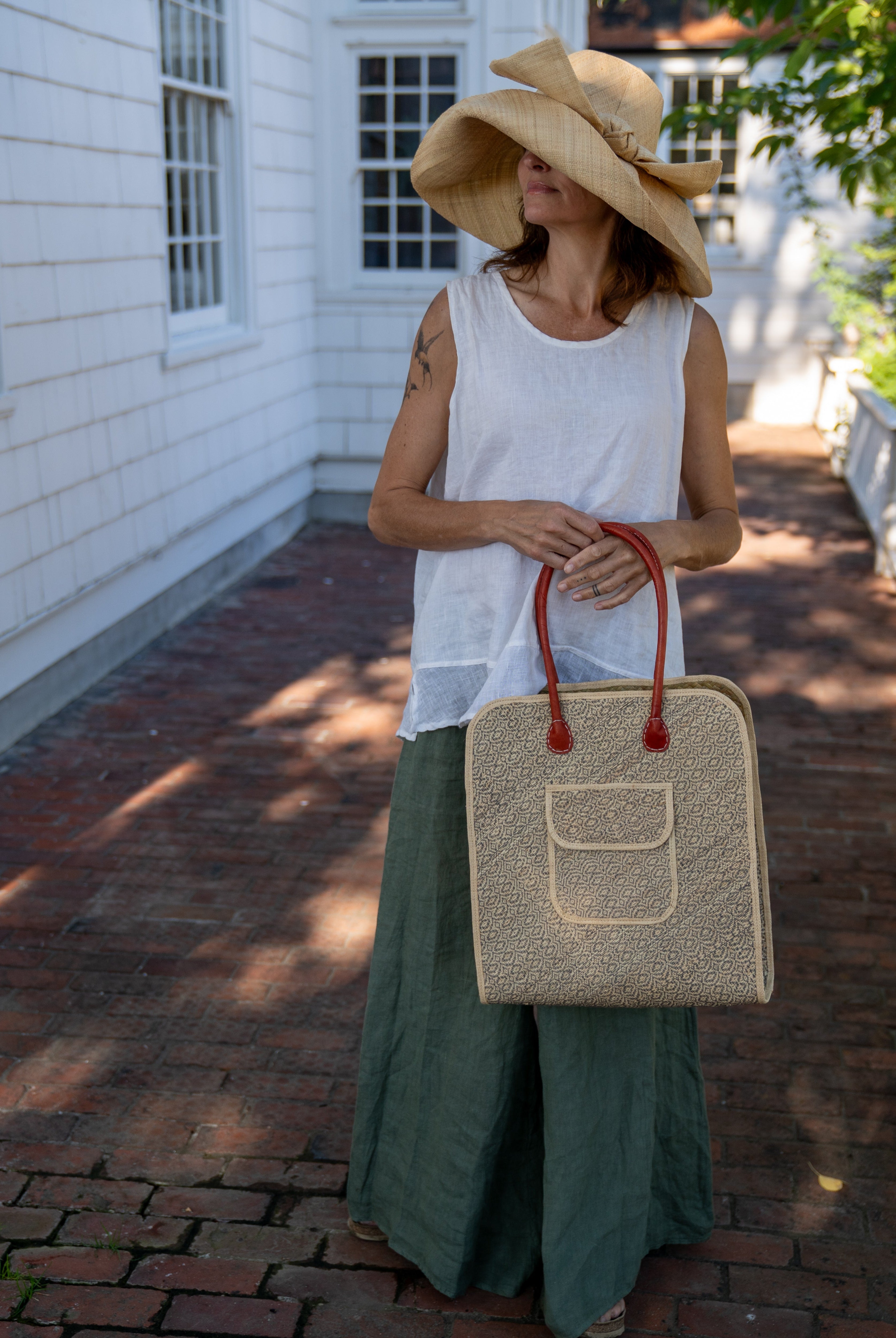 Model wearing Josephine 50's Inspired Woven Straw Handbag handmade natural raffia palm fiber in natural straw color woven with contrasting Grey thread stitching in a subtle diagonal stripe pattern consisting of bands of ovals and circles with loomed raffia edging around the bag as well as the pocket and flap of the exterior pocket - Shebobo (with Audrey 5" & 7" Wide Brim Big Bow Solid Color Packable Straw Sun Hats)