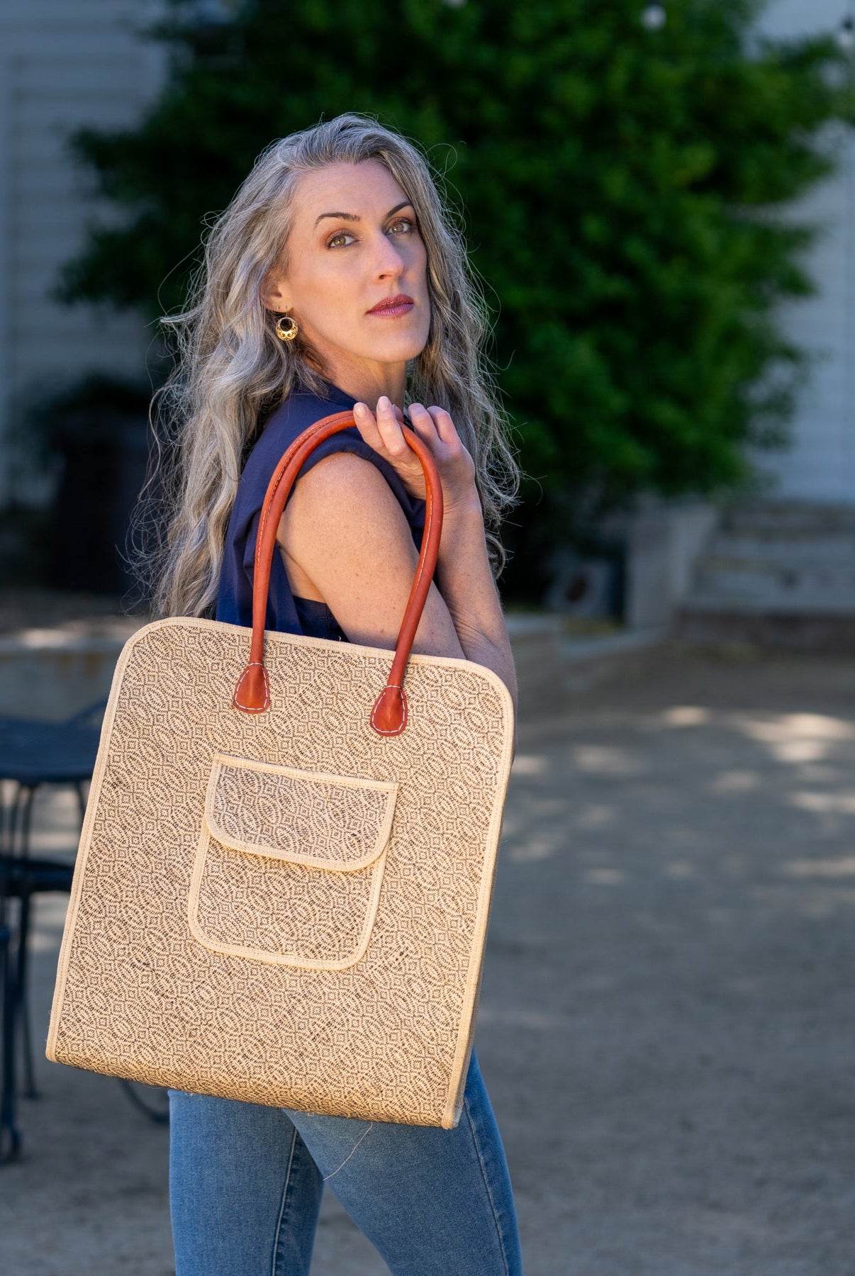 Model wearing Josephine 50's Inspired Woven Straw Handbag handmade natural raffia palm fiber in natural straw color woven with contrasting Black thread stitching in a subtle diagonal stripe pattern consisting of bands of ovals and circles with loomed raffia edging around the bag as well as the pocket and flap of the exterior pocket - Shebobo