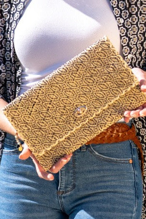 Model wearing Josephine Woven Straw Clutch Purse handmade natural raffia palm fiber in natural straw color woven with contrasting black thread stitching in a subtle diagonal stripe pattern consisting of bands of ovals and circles handbag with crosshatch stitch edging - Shebobo