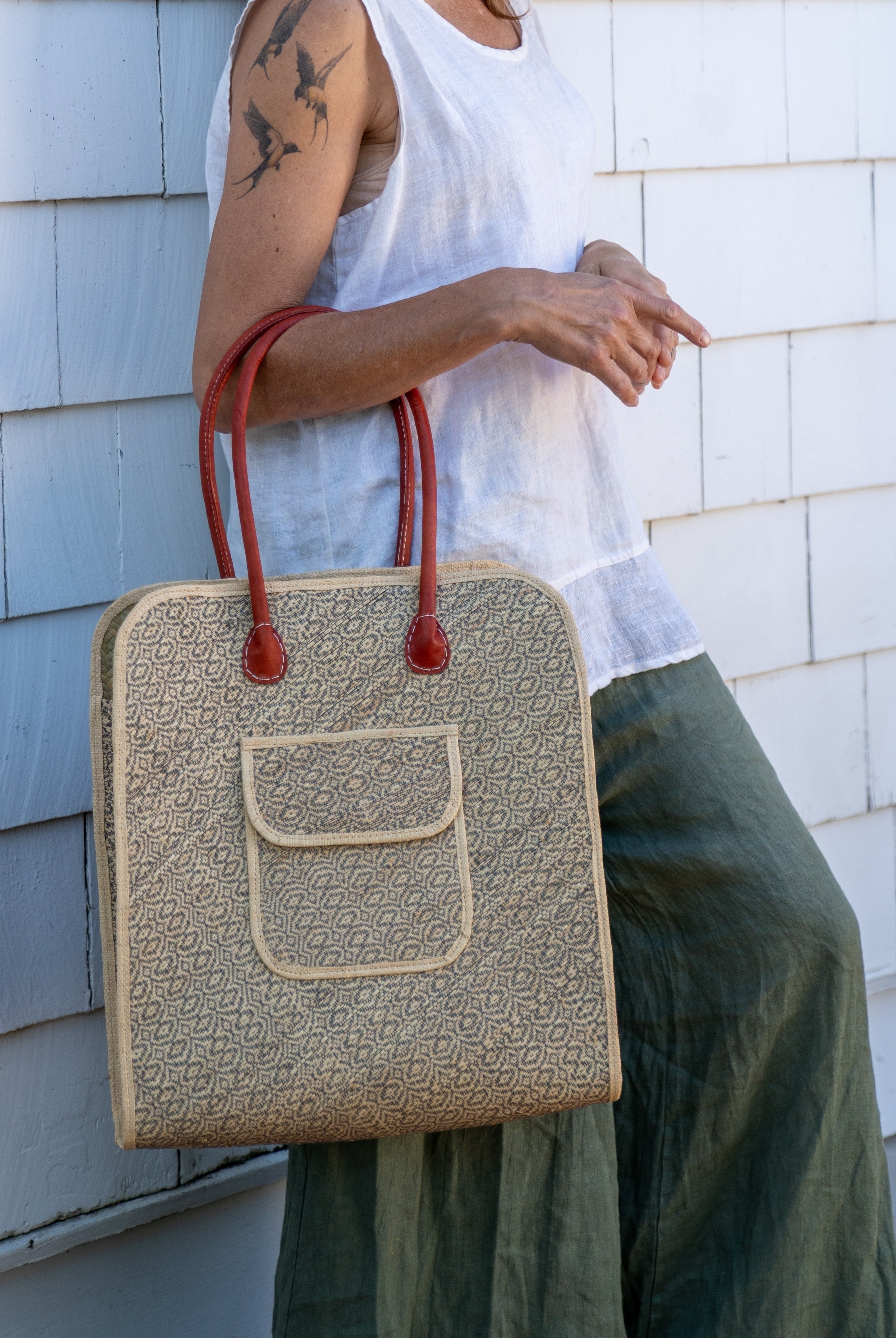 Model wearing Josephine 50's Inspired Woven Straw Handbag handmade natural raffia palm fiber in natural straw color woven with contrasting Grey thread stitching in a subtle diagonal stripe pattern consisting of bands of ovals and circles with loomed raffia edging around the bag as well as the pocket and flap of the exterior pocket - Shebobo