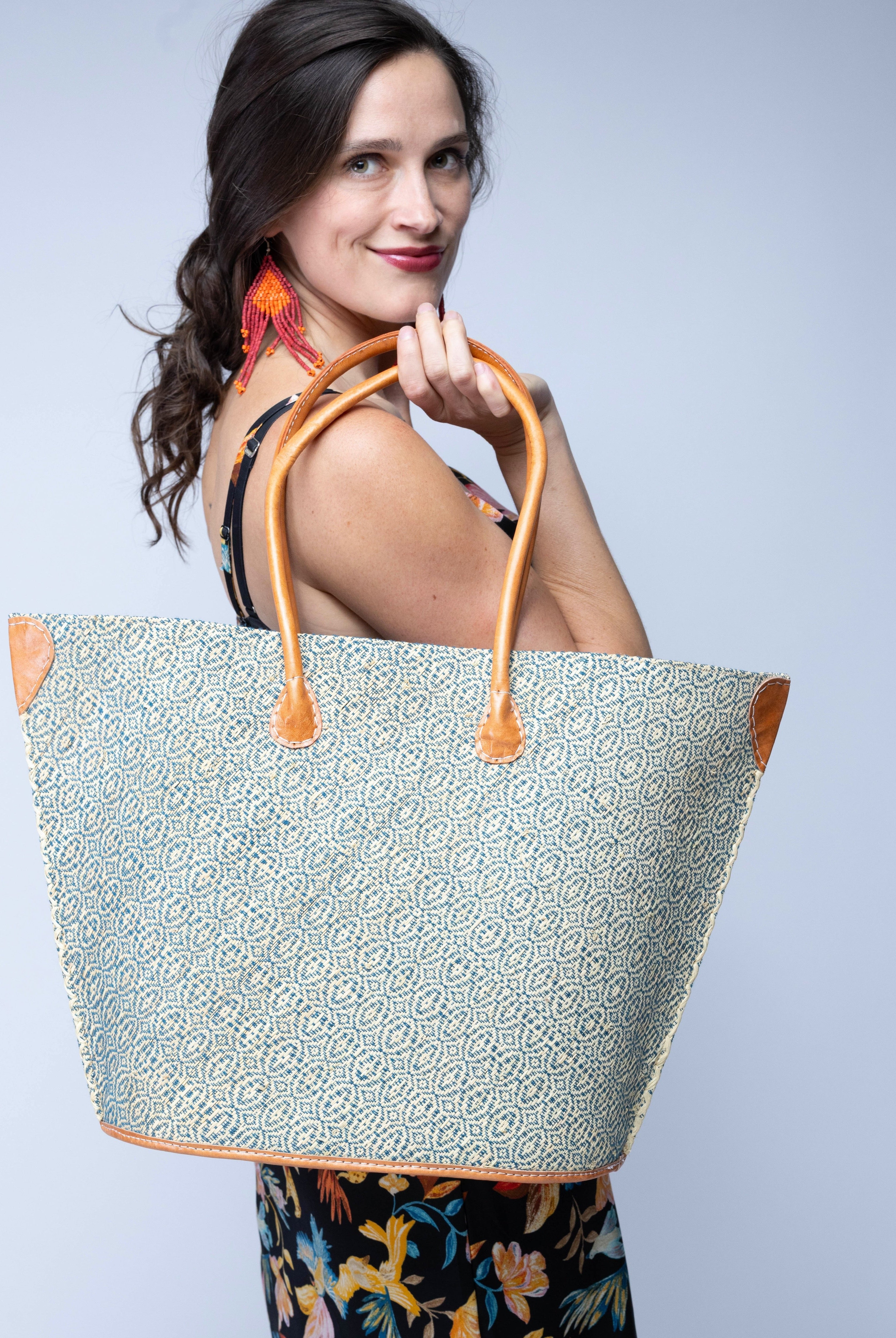 Model wearing Josephine Woven Small Straw Tote Bag handmade natural raffia palm fiber in natural straw color woven with contrasting Turquoise blue/green thread stitching in a subtle diagonal stripe pattern consisting of bands of ovals and circles with natural cross-stitch edge and leather handles beach bag shoulder bag - Shebobo