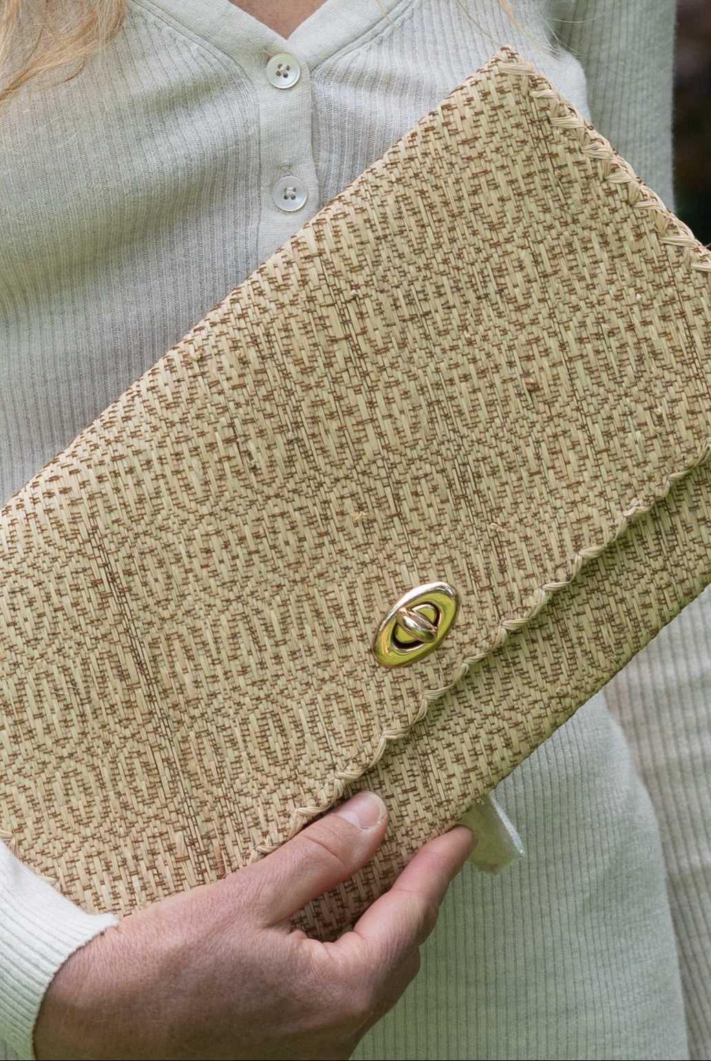 Model wearing Josephine Woven Straw Clutch Purse handmade natural raffia palm fiber in natural straw color woven with contrasting cinnamon tobacco/dark/brown thread stitching in a subtle diagonal stripe pattern consisting of bands of ovals and circles handbag with crosshatch stitch edging - Shebobo