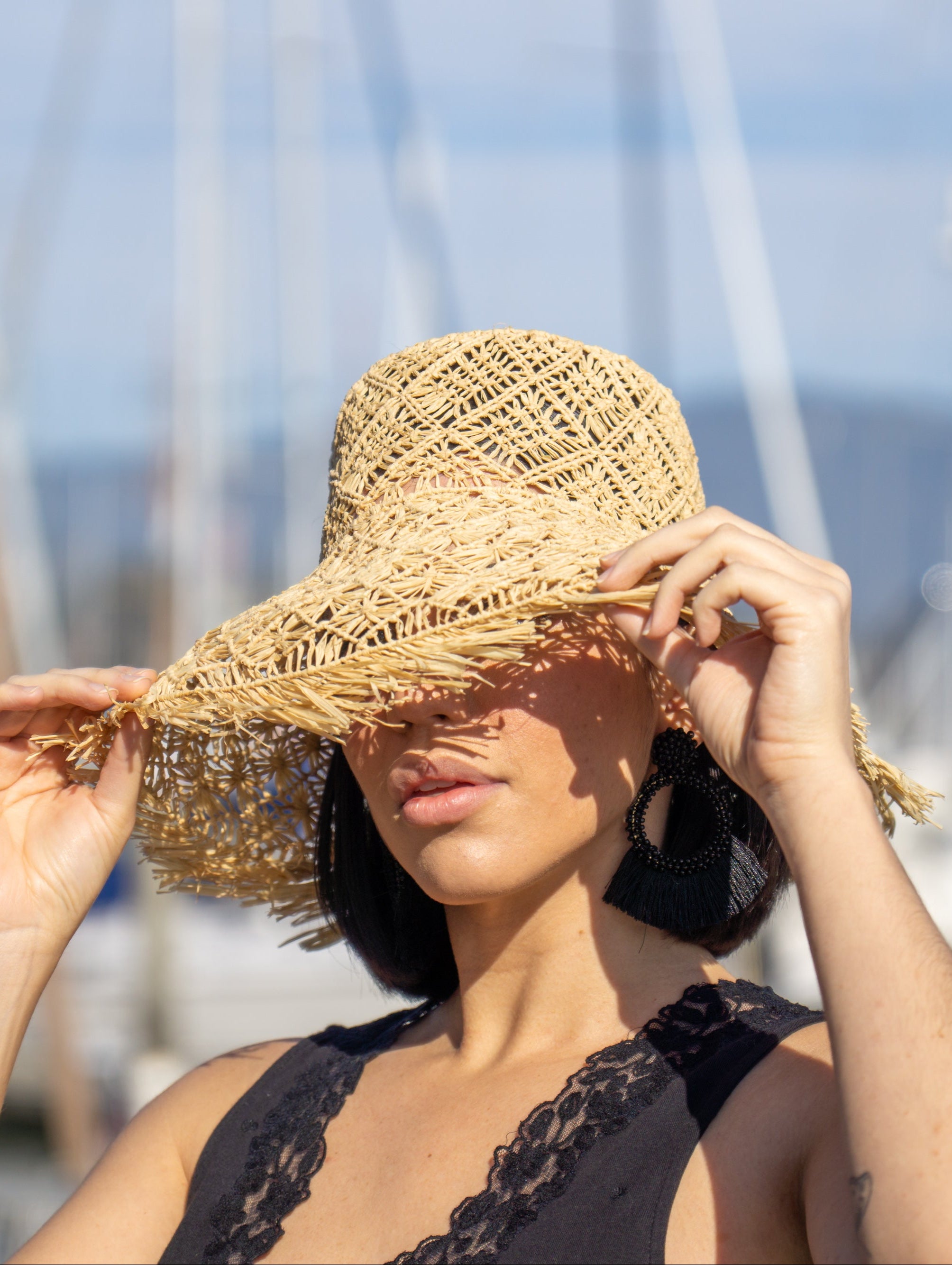 Model wearing Karin Crochet & Macrame Natural Raffia Knotted Straw Sun Hat Lightweight Breathable with Fringe Edge geometric star or sunburst design brim and geometric knotted diamond pattern top - Shebobo