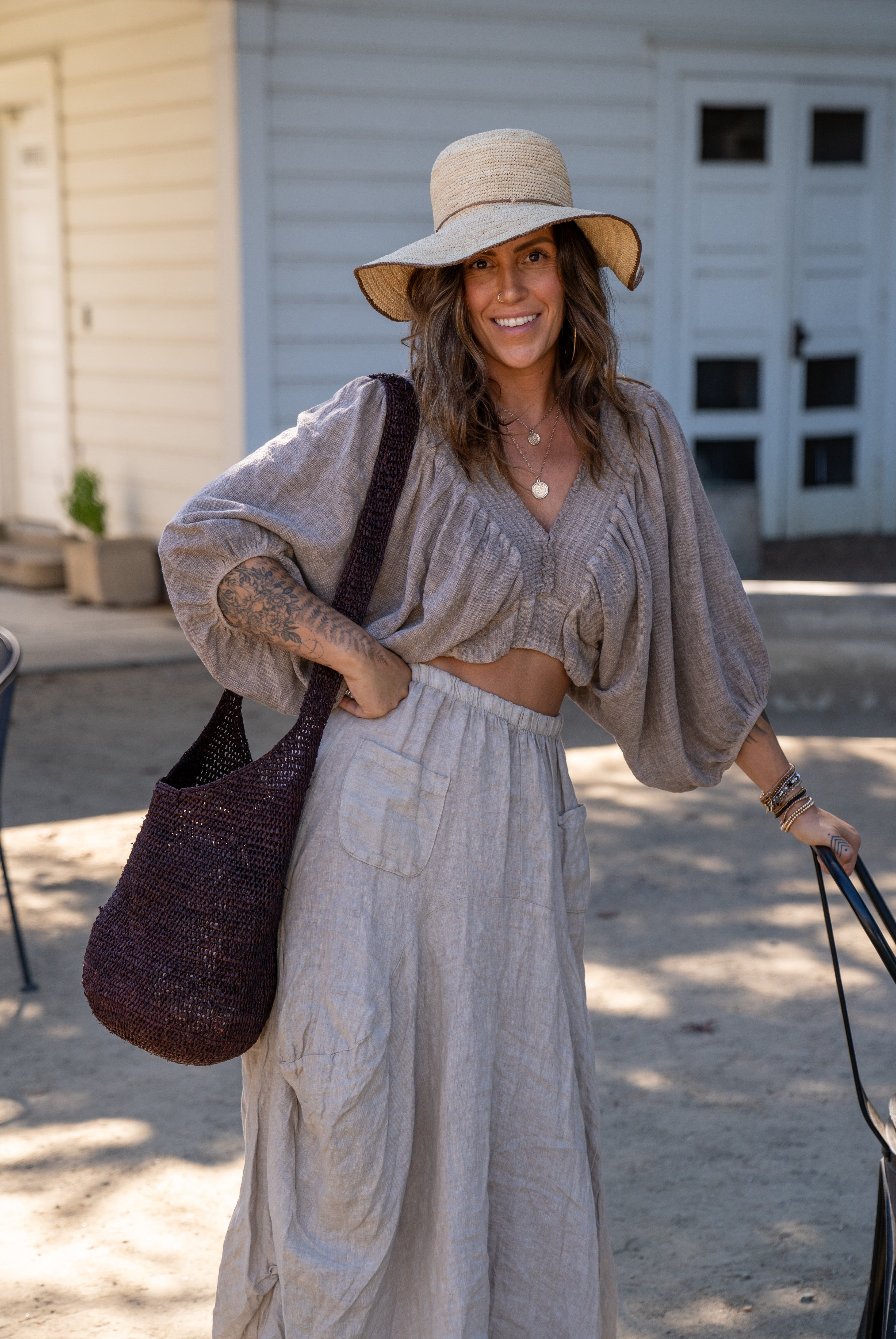 Model wearing Model wearing Kiki Crochet Straw Crossbody Bag handmade natural raffia palm fiber in a crochet pattern of subtle linked bands in a solid hue of dark chocolate brown purse - Shebobo (with Rachel 4" Brim Crochet Straw Sun Hats with Colored Edge)