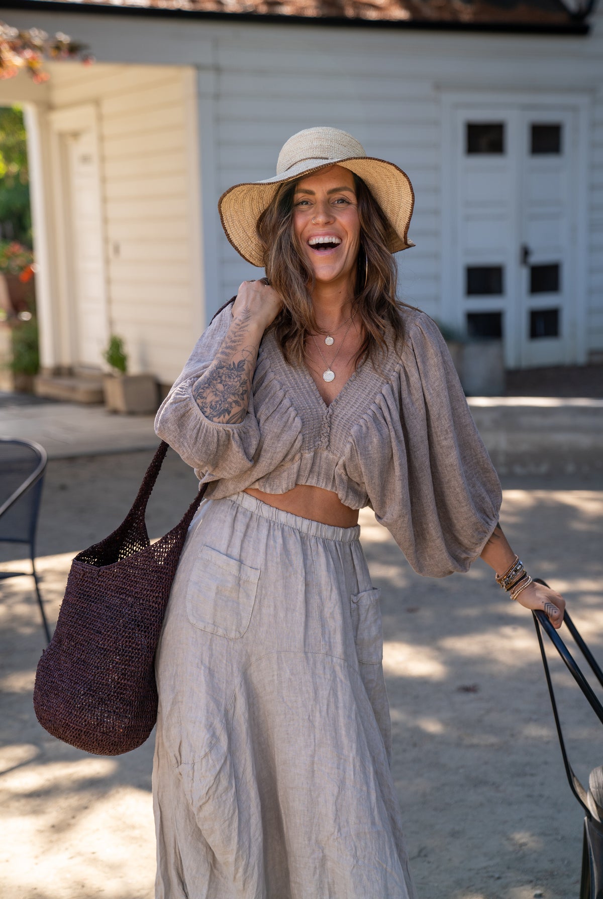 Model wearing Model wearing Kiki Crochet Straw Crossbody Bag handmade natural raffia palm fiber in a crochet pattern of subtle linked bands in a solid hue of dark chocolate brown purse - Shebobo (with Rachel 4" Brim Crochet Straw Sun Hats with Colored Edge)