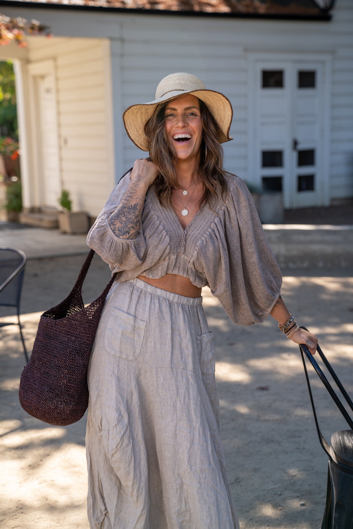Model wearing Model wearing Kiki Crochet Straw Crossbody Bag handmade natural raffia palm fiber in a crochet pattern of subtle linked bands in a solid hue of dark chocolate brown purse - Shebobo (with Rachel 4" Brim Crochet Straw Sun Hats with Colored Edge)