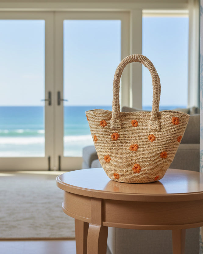 Lifestyle view Kirra Daisy Flowers Crochet Straw Basket Handbag handmade crochet raffia palm fiber in a solid hue of natural straw color with embroidered round saffron yellow/orange petals and coral orange/red inner dot flower pattern purse with matching crochet handles beach bag purse tote - Shebobo