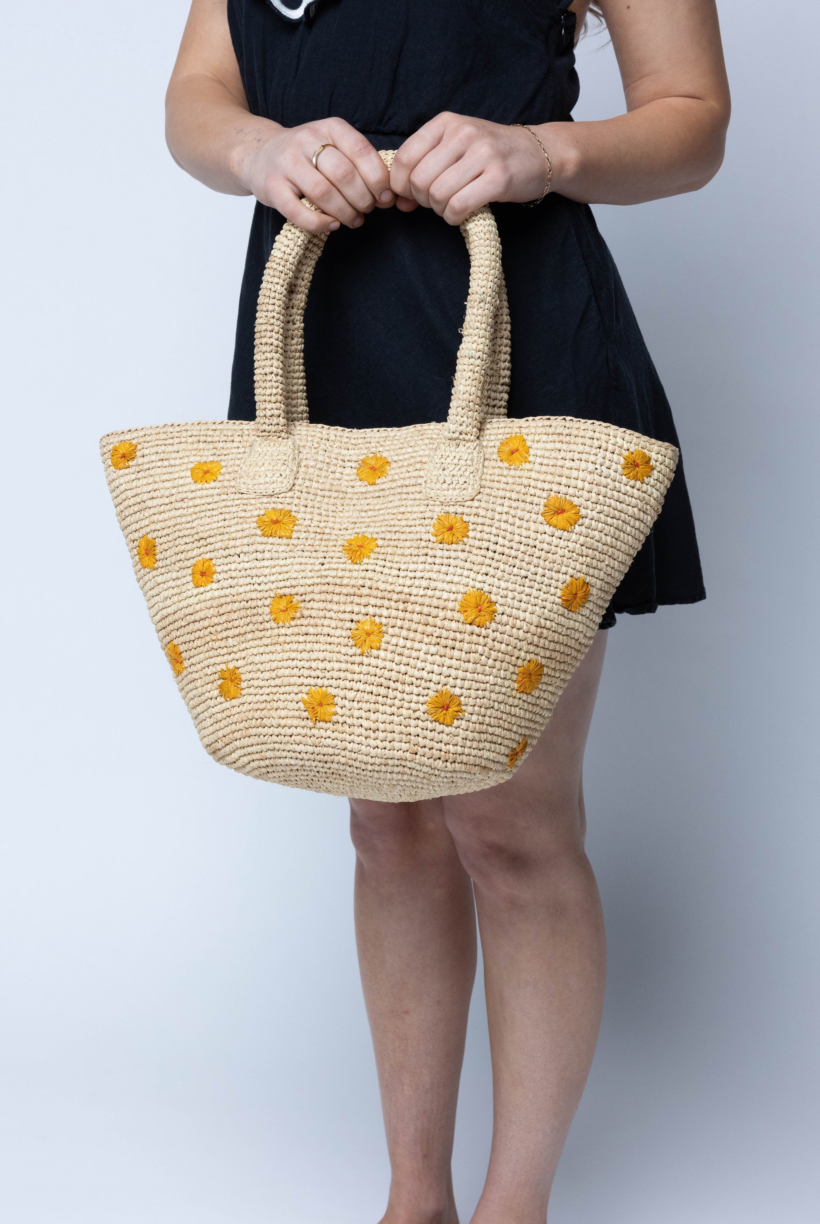 Model wearing Kirra Daisy Flowers Crochet Straw Basket Handbag handmade crochet raffia palm fiber in a solid hue of natural straw color with embroidered round saffron yellow/orange petals and coral orange/red inner dot flower pattern purse with matching crochet handles beach bag purse tote - Shebobo