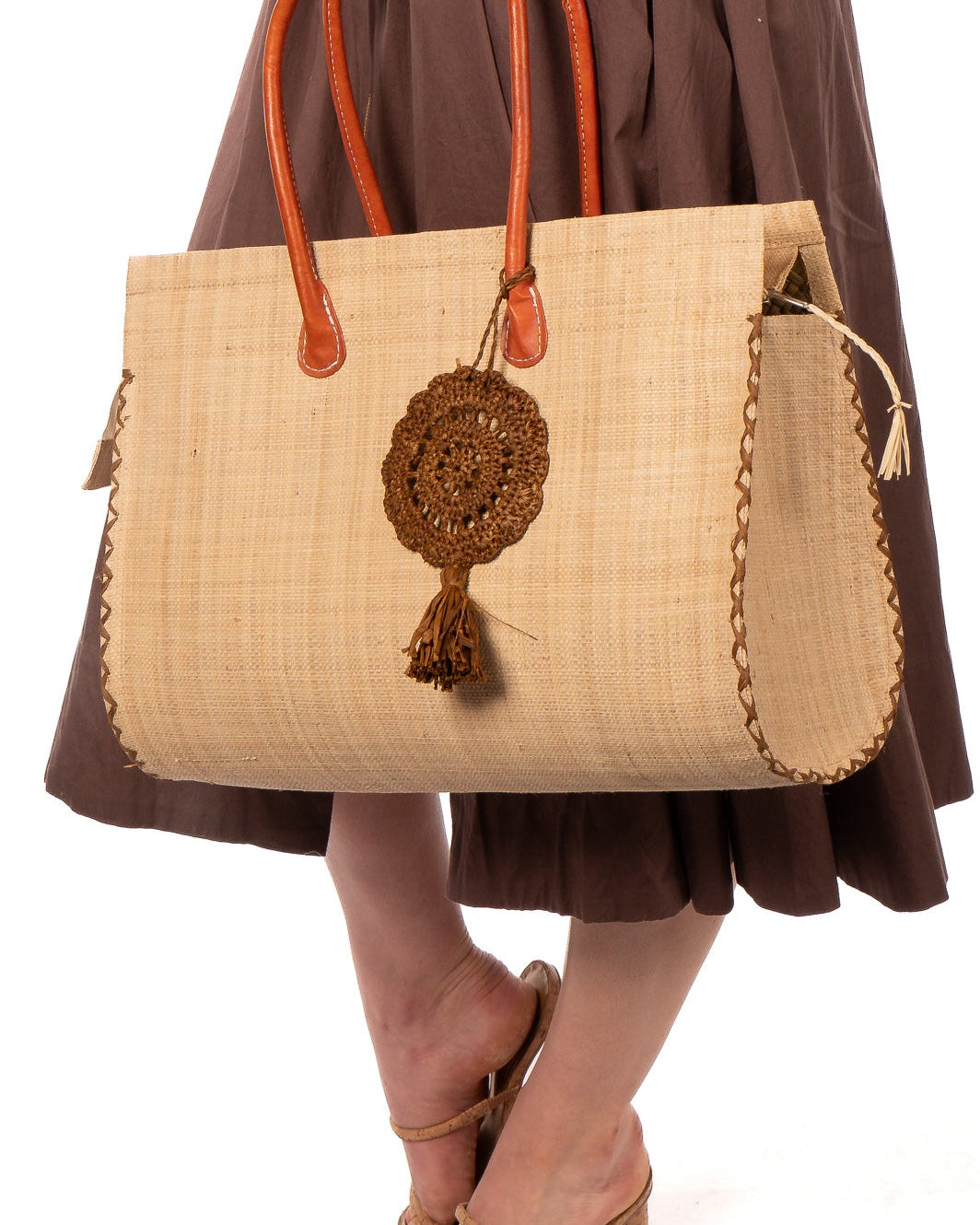 Model wearing Lace Pattern Dreamcatcher Crochet Raffia Straw Tassel Charm Embellishment handmade natural raffia palm fiber in a solid hue of Tobacco cinnamon/dark/brown in a woven lace style disc with two concentric rings of open circular pattern in the center and scalloped outer edge with matching twist loop and brushed fringe tassel - Shebobo