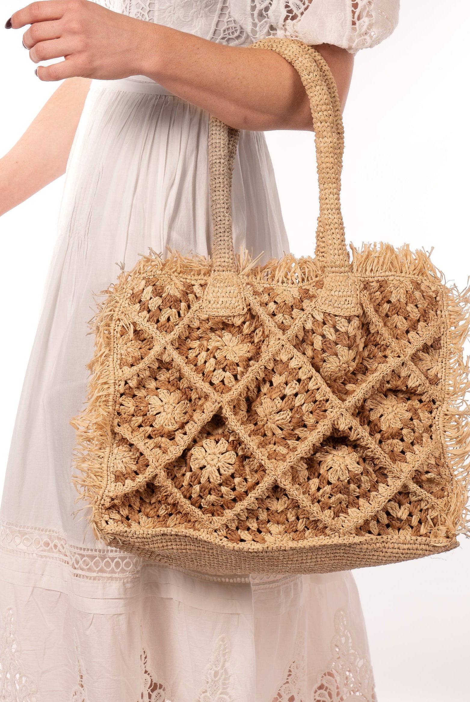 Model wearing Leo Crochet Granny Square Pattern Handbag with Fringe Edge handmade woven raffia palm fiber in a two tone cappuccino light/brown/beige and natural straw color multicolor pattern of woven granny squares oriented on the diagonal with natural raw fringe edging and handles basket bag - Shebobo