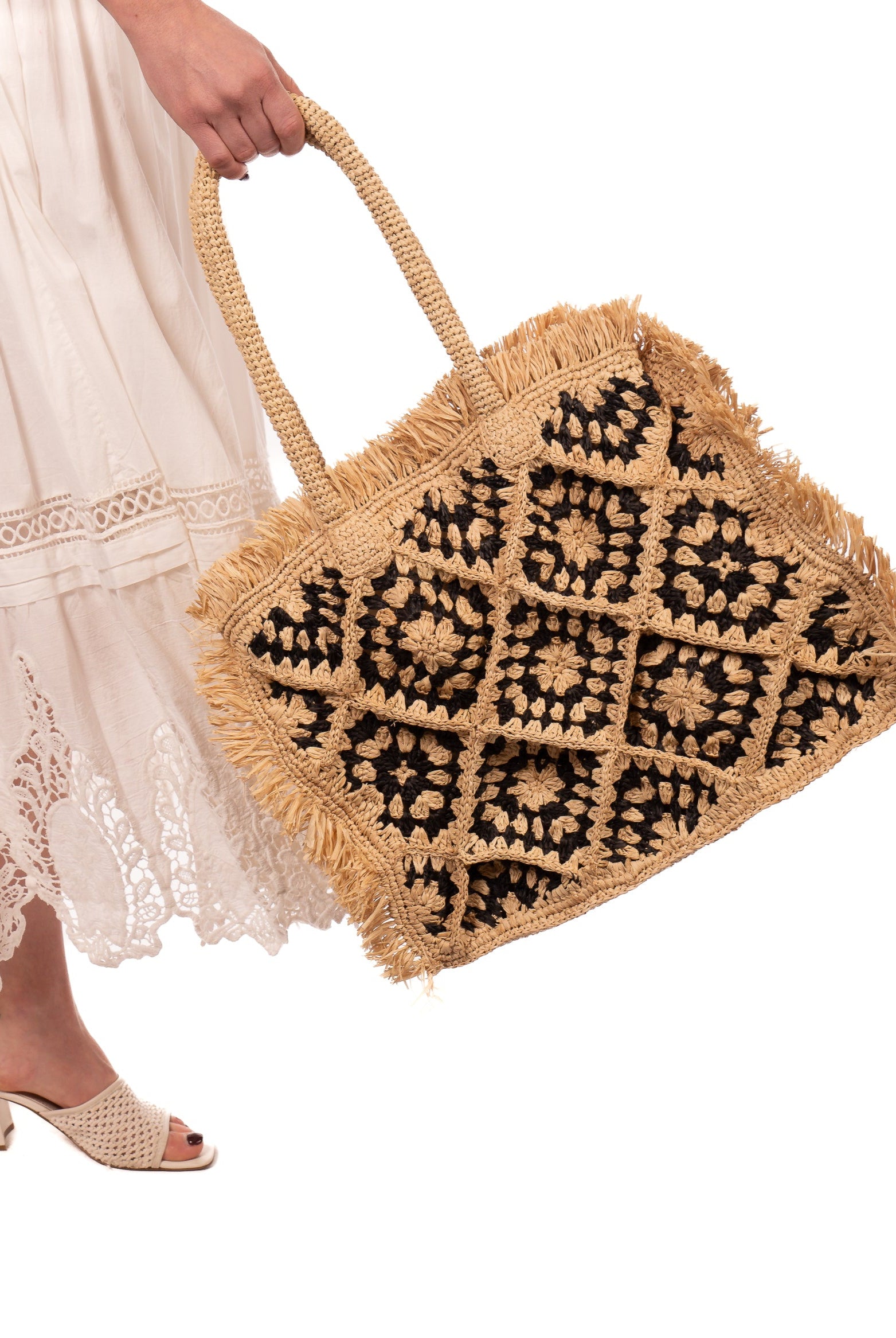 Model wearing Leo Crochet Granny Square Pattern Handbag with Fringe Edge handmade woven raffia palm fiber in a two tone black and natural straw color multicolor pattern of woven granny squares oriented on the diagonal with natural raw fringe edging and handles basket bag - Shebobo