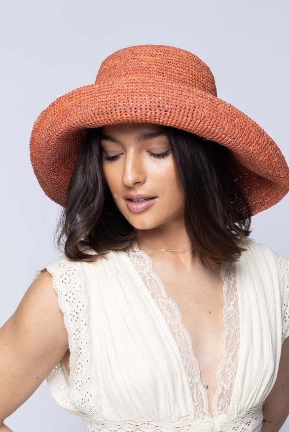 Model wearing Leor Blush crochet straw hat handmade woven natural raffia palm fiber in a solid hue of blush pink/orange raffia 3" brim packable straw hat with matching adjustable braided hat band - Shebobo