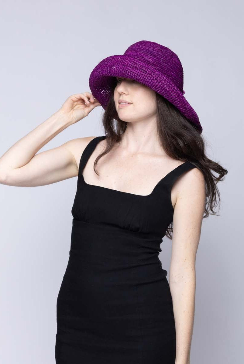 Model wearing Leor Moxi crochet straw hat handmade woven natural raffia palm fiber in a solid hue of Moxi deep/purple raffia 3" brim packable straw hat with matching adjustable braided hat band - Shebobo