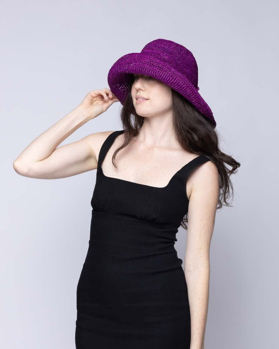 Model wearing Leor Moxi crochet straw hat handmade woven natural raffia palm fiber in a solid hue of Moxi deep/purple raffia 3" brim packable straw hat with matching adjustable braided hat band - Shebobo