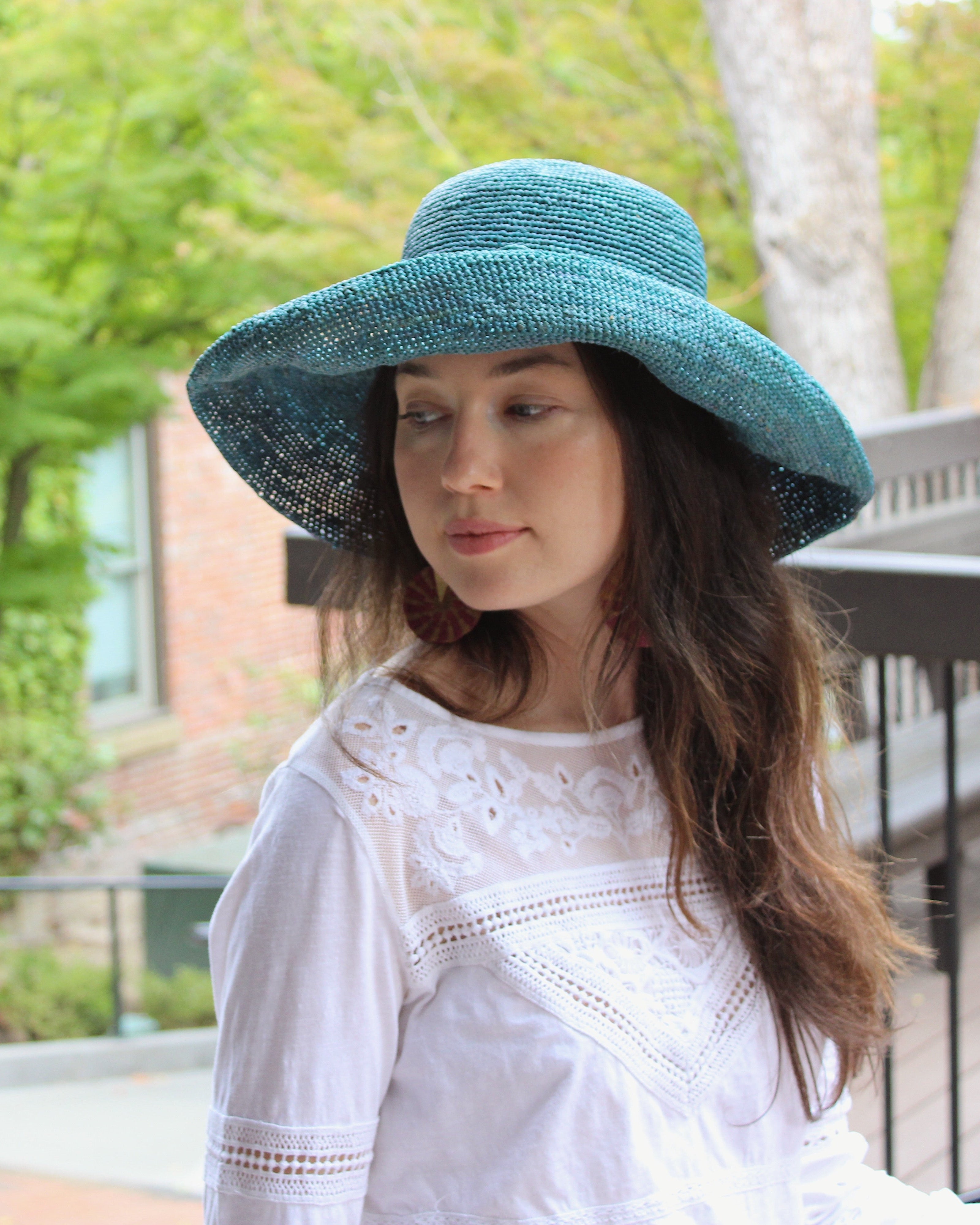 Model wearing Leor Turquoise crochet straw hat handmade woven natural raffia palm fiber in a solid hue of turquoise blue/green raffia 3" brim packable straw hat with matching adjustable braided hat band - Shebobo
