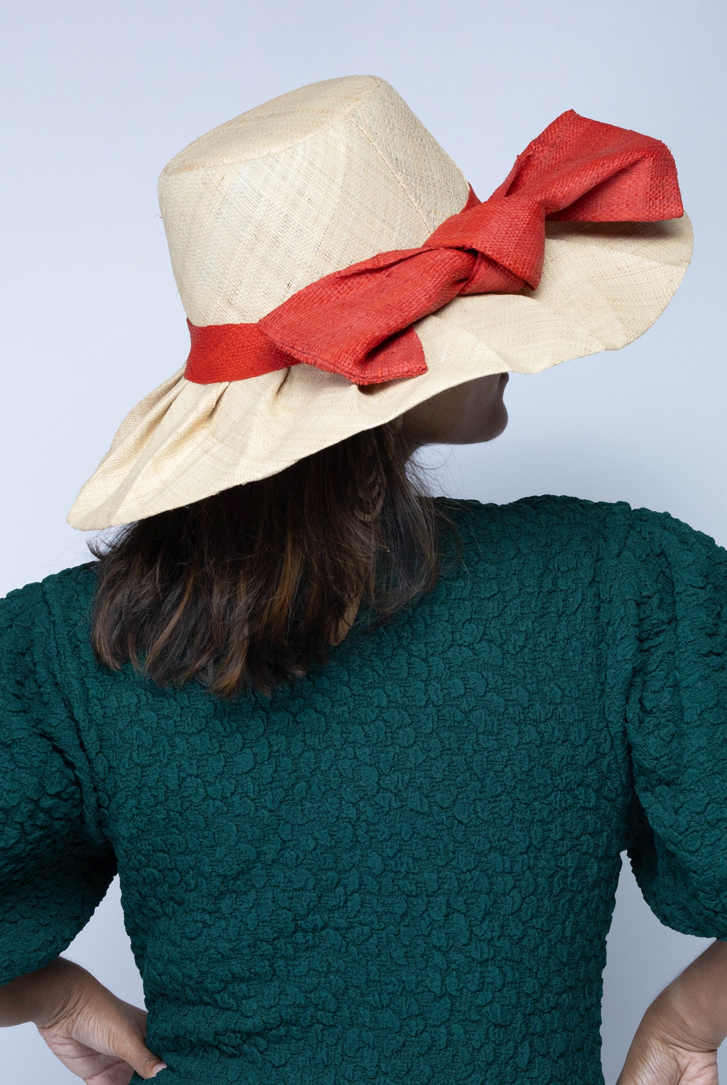 Model wearing Lilly 5" Brim Fan Straw Sun Hat with Big Coral orange/red bow and matching hatband on handmade natural loomed raffia pleated wide brim hat - Shebobo