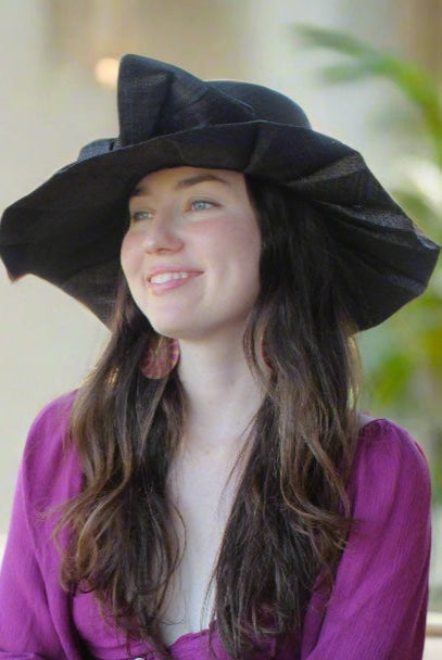 Model wearing Lilly 5" Brim Fan Straw Sun Hat with Big Bow Black handmade loomed natural raffia palm fiber in a solid hue of black with pleated wide brim and oversized bow embellishment - Shebobo